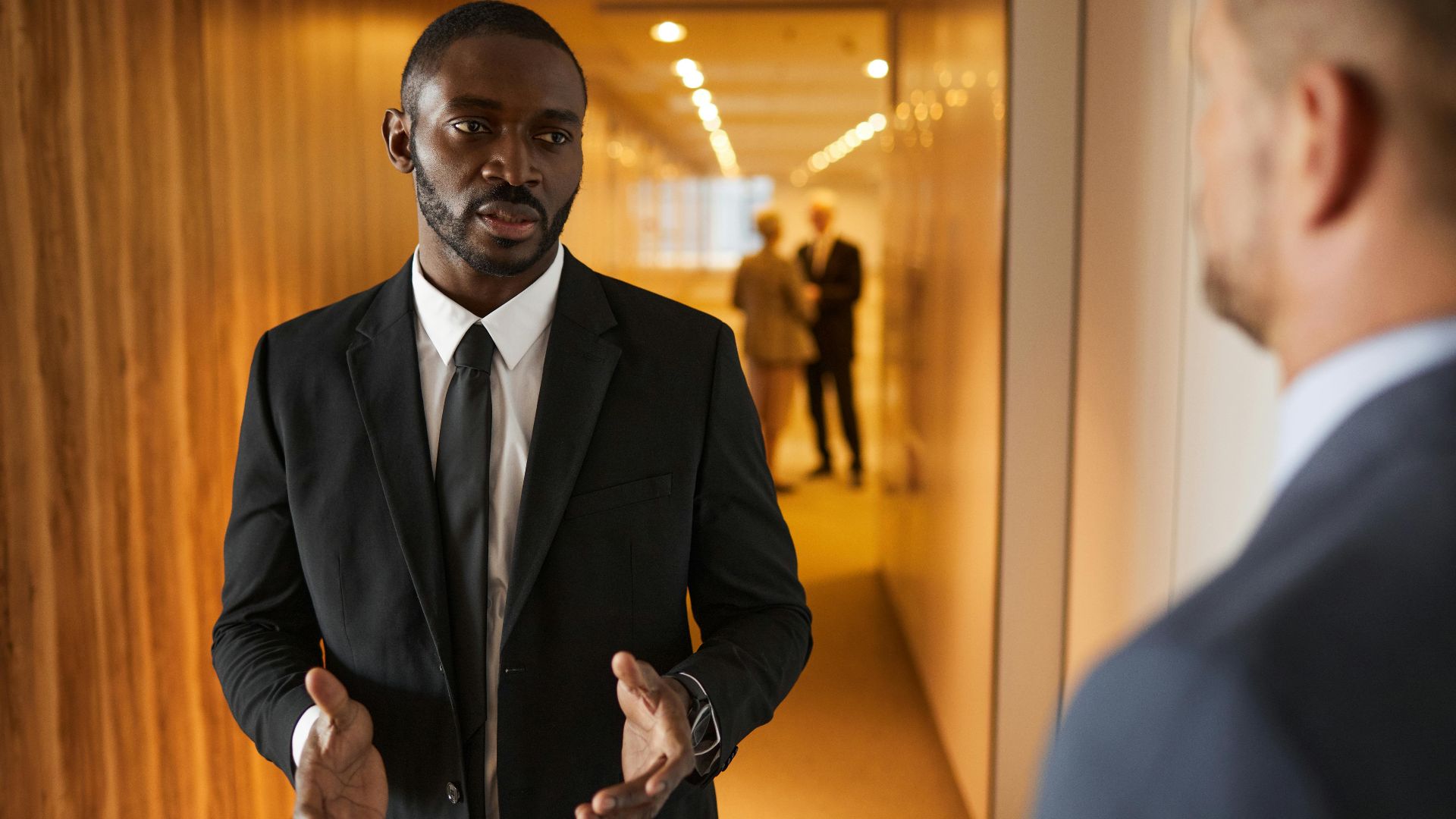 Business professionals in suits having a conversation in a modern office hallway.