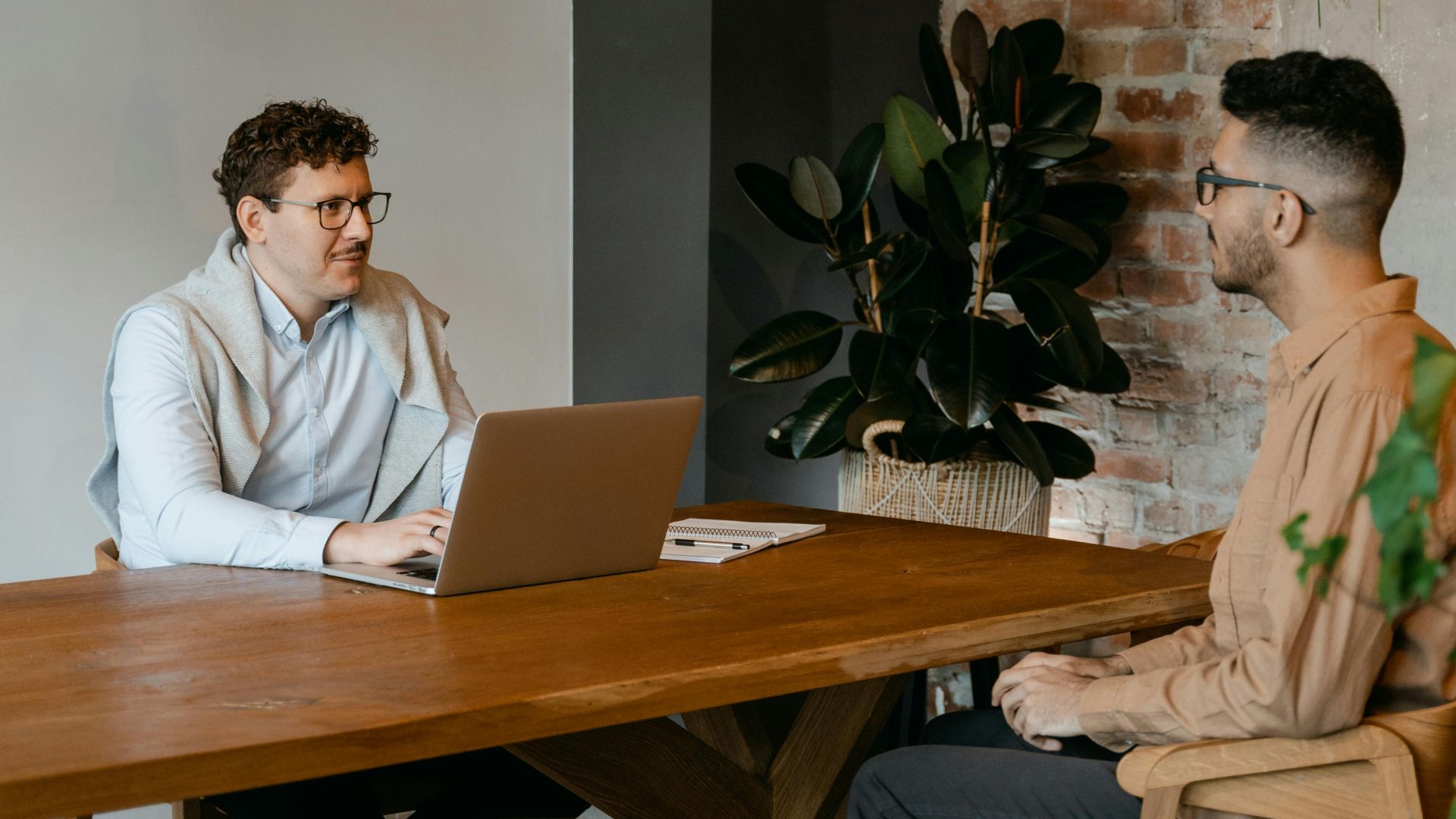 Two men engaged in a business conversation at a wooden table in a stylish office.