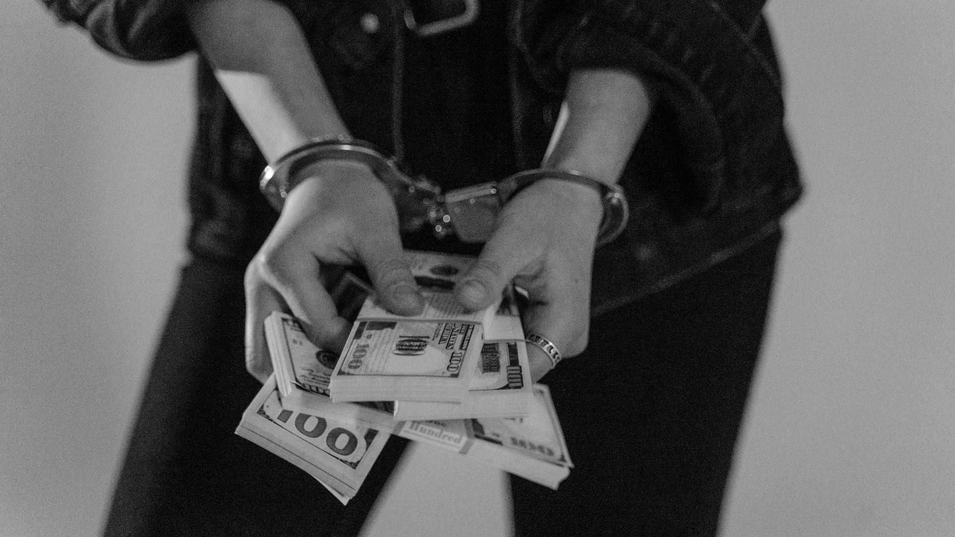 Black and white image of a handcuffed person holding bundles of US dollars.