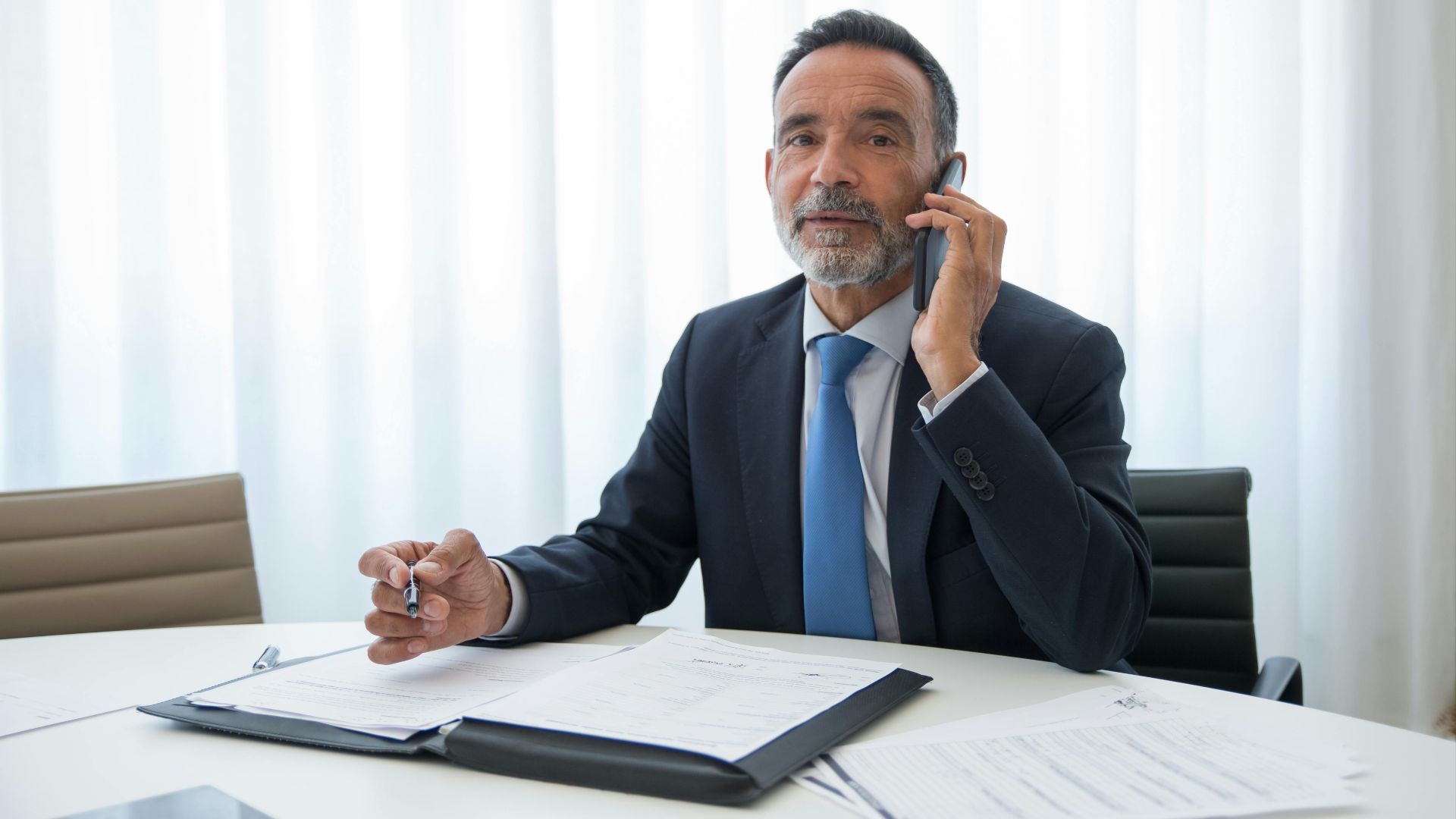 Senior businessman in suit discussing important documents on the phone at an office room.