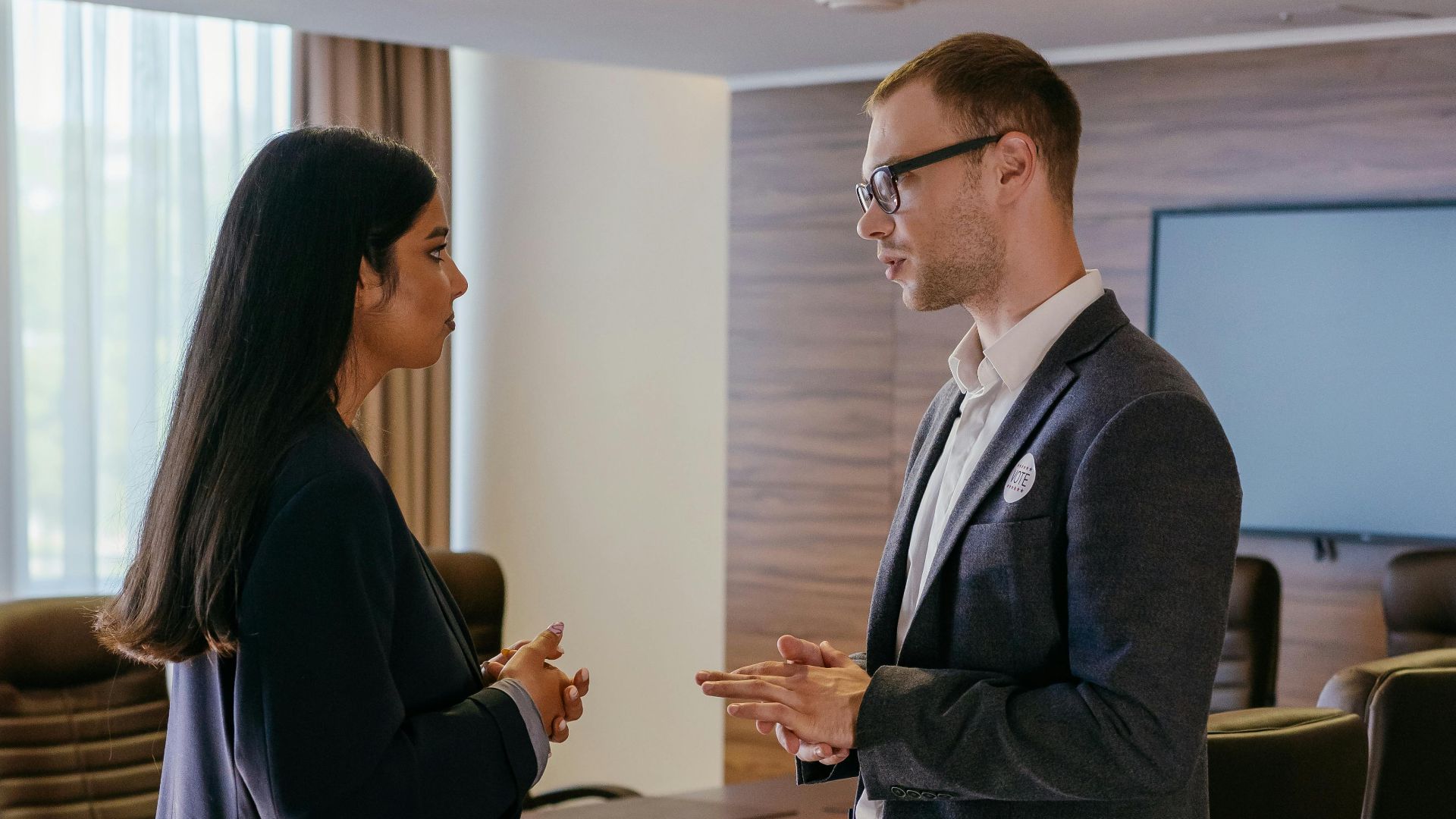Two professionals engaged in discussion inside a modern conference room setting.