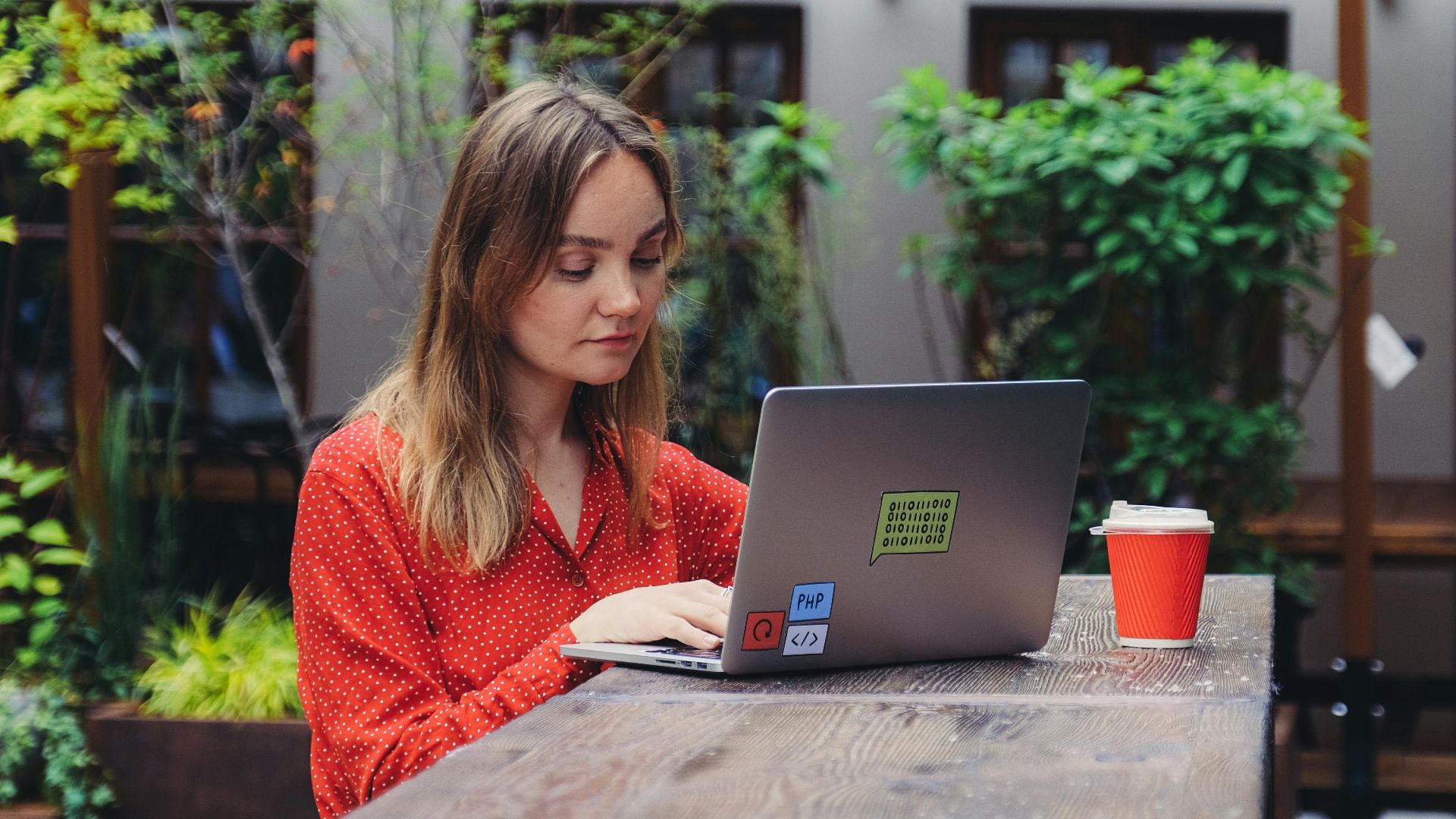 Young woman working on a laptop in an outdoor cafe setting, enjoying a cup of coffee.