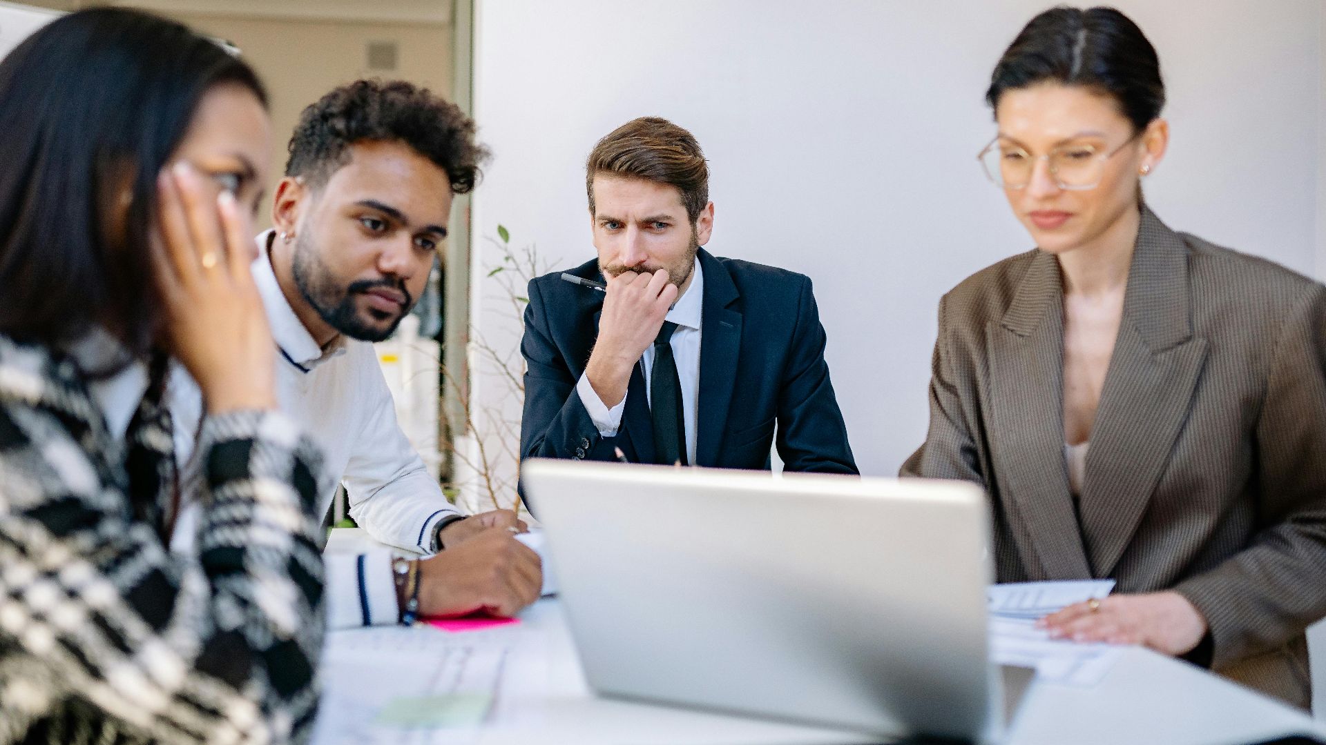 Focused team of professionals discussing work at a laptop during an office meeting.
