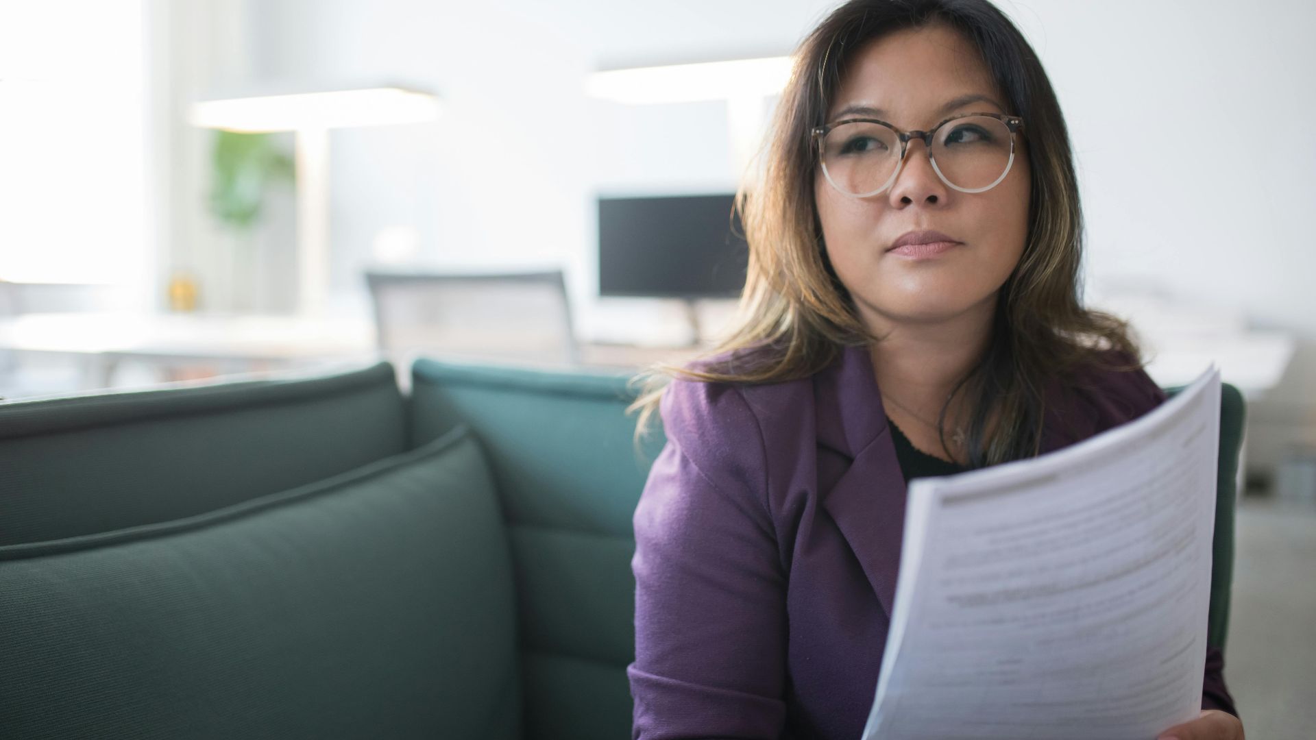 Asian businesswoman in office holding documents, expressing confidence and professionalism.