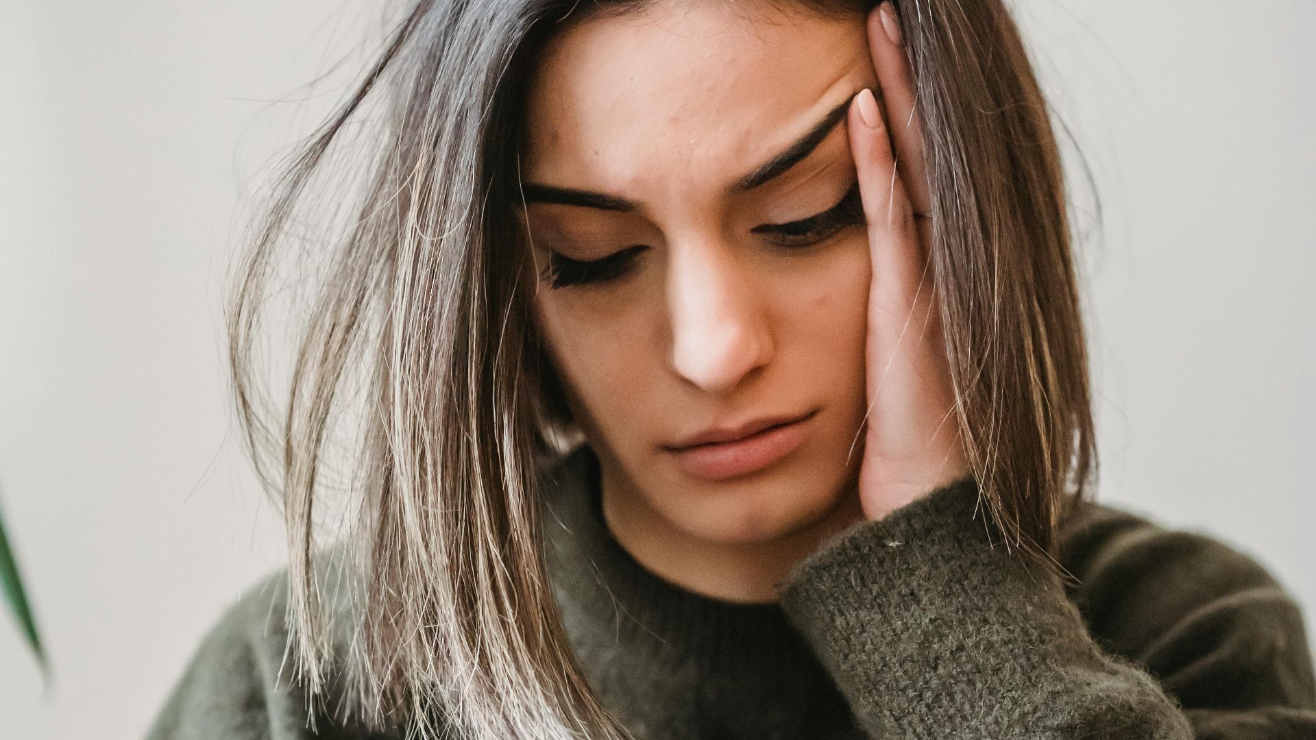 Unhappy female in casual wear leaning on hand and surfing internet on cellphone while sitting in light room near wall at home