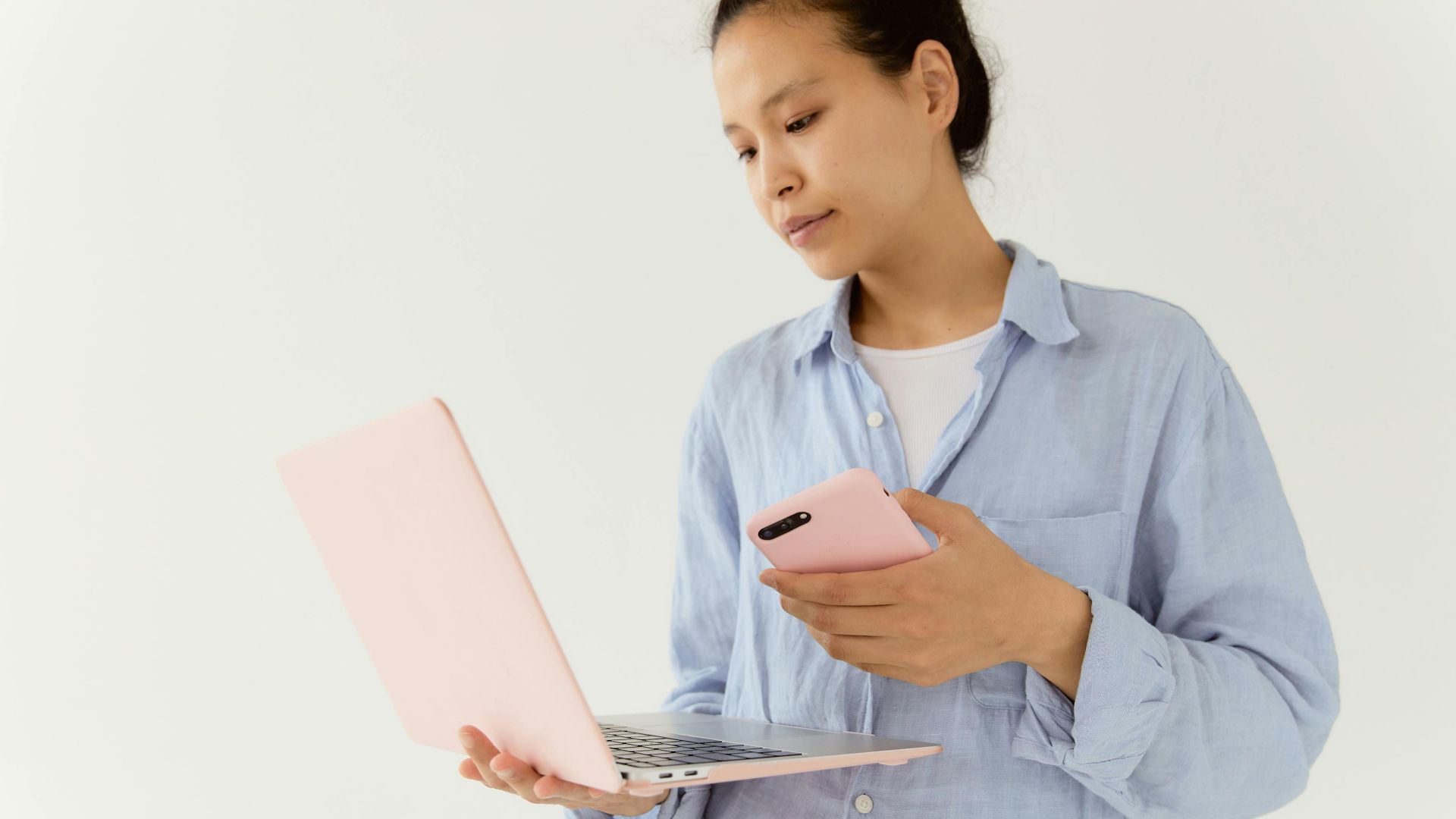 Asian woman engaging with technology using a laptop and smartphone indoors.