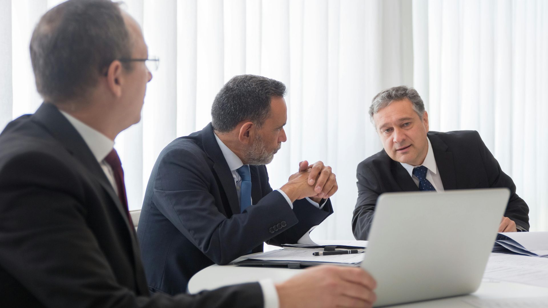 Three businessmen collaborating during a meeting around a laptop in a bright office.