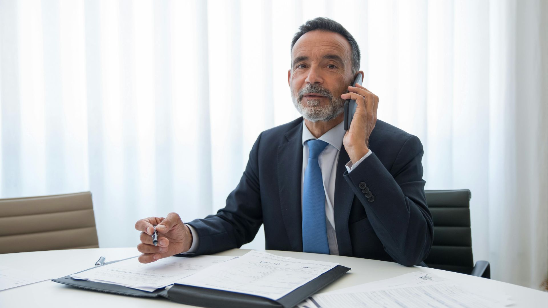 Senior businessman in suit discussing important documents on the phone at an office room.
