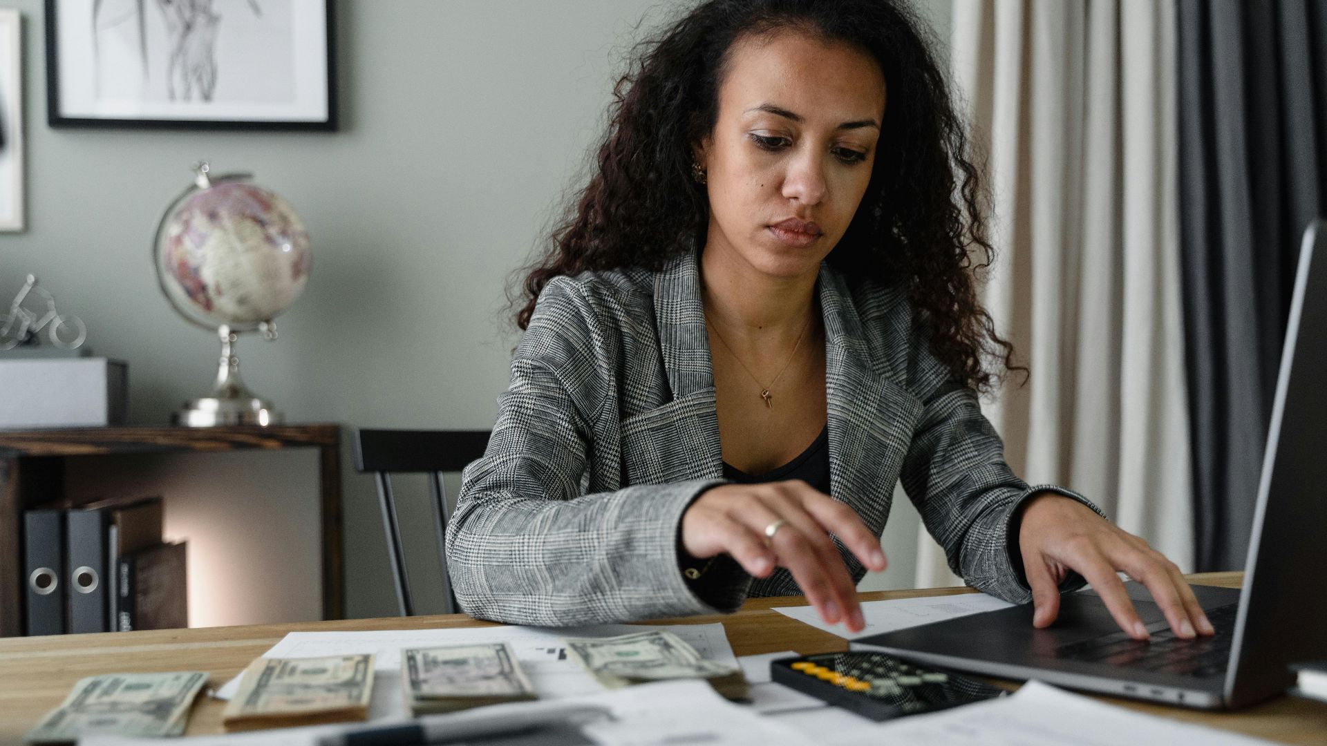 Professional woman analyzing financial documents and counting cash at office desk.