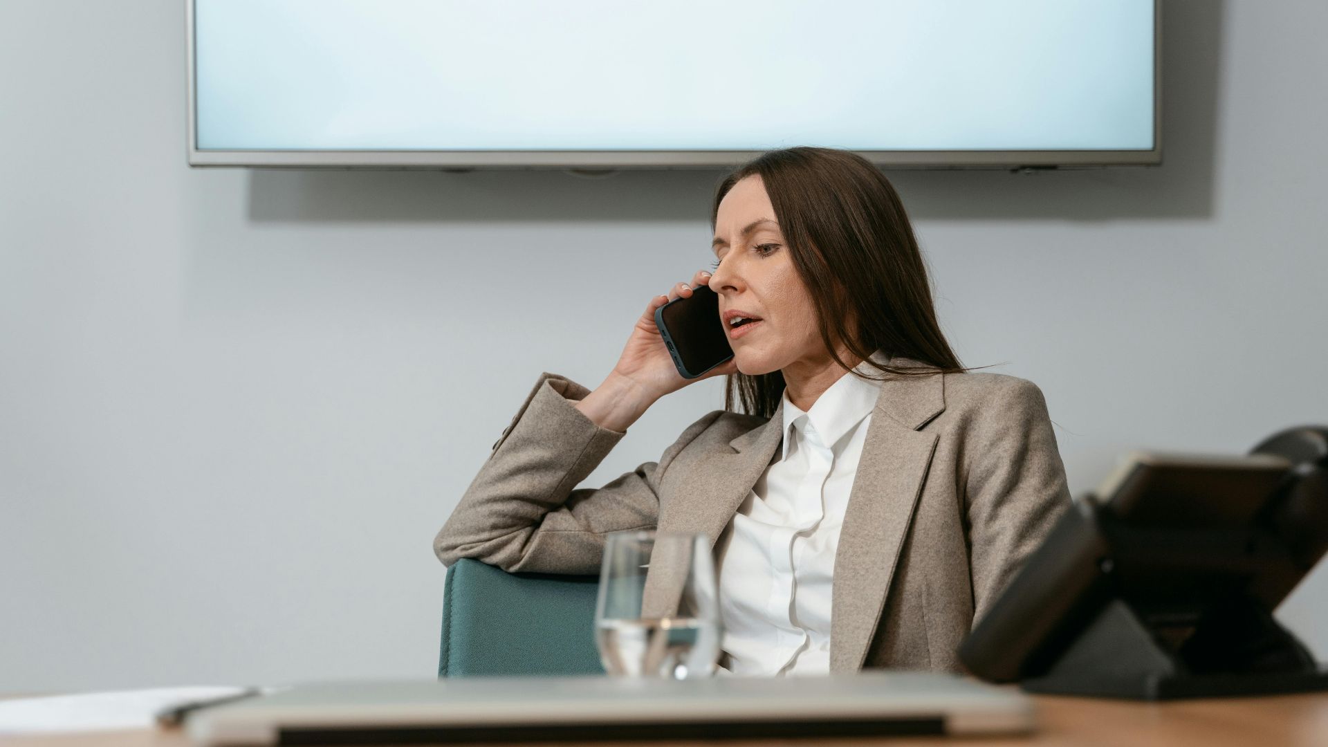 Businesswoman in a blazer making a phone call in an office setting, engaging in a conversation.