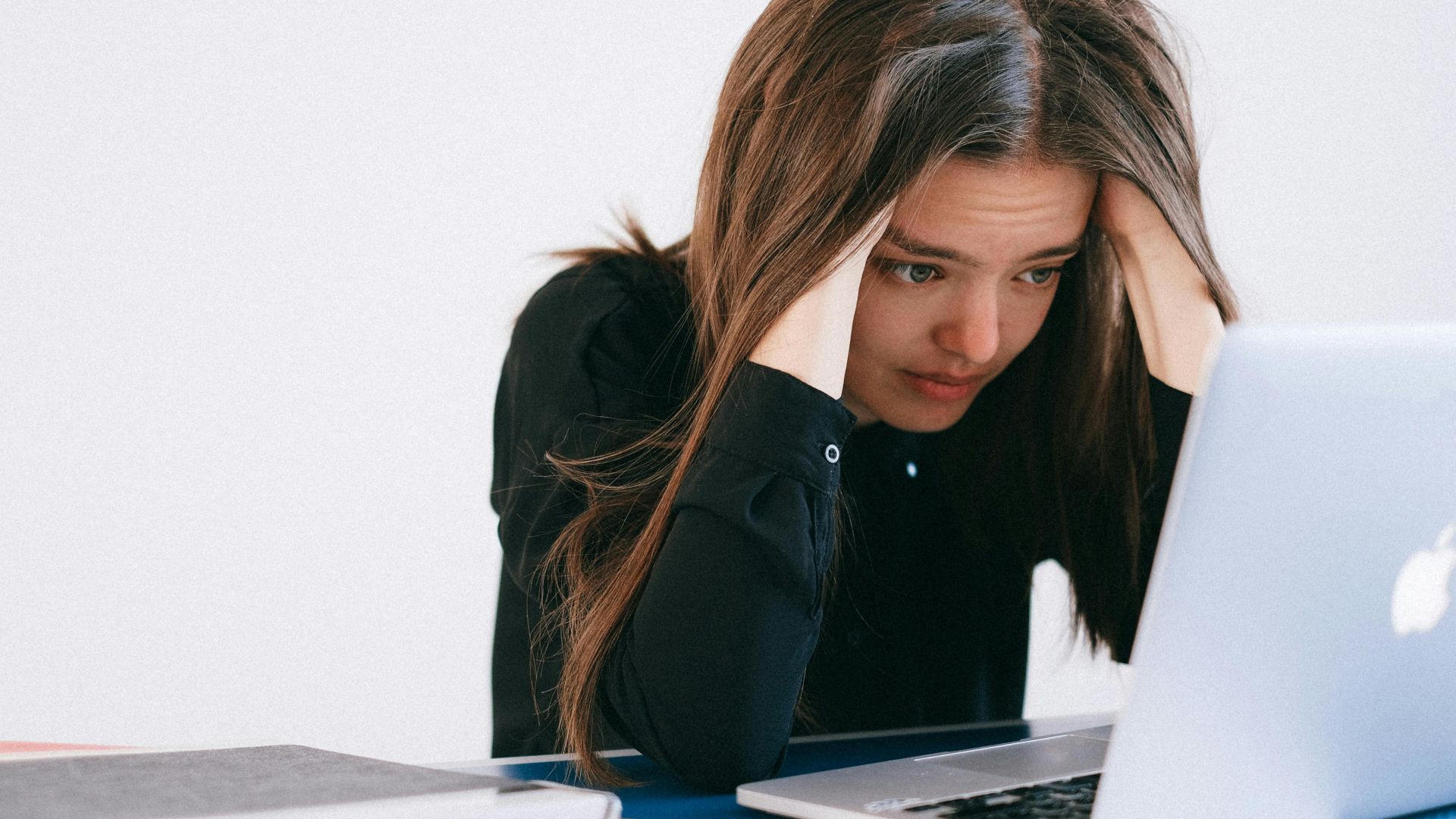 A stressed woman at a desk, looking at a laptop with a worried expression.