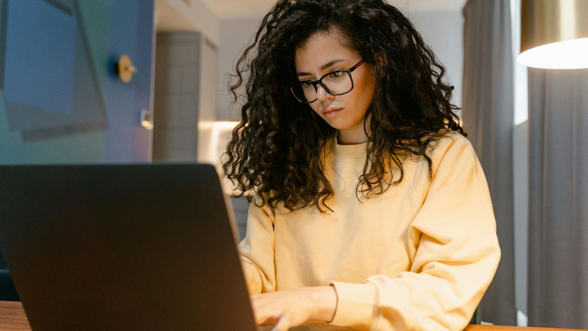 Woman in yellow sweater working on a laptop in a cozy home setting.