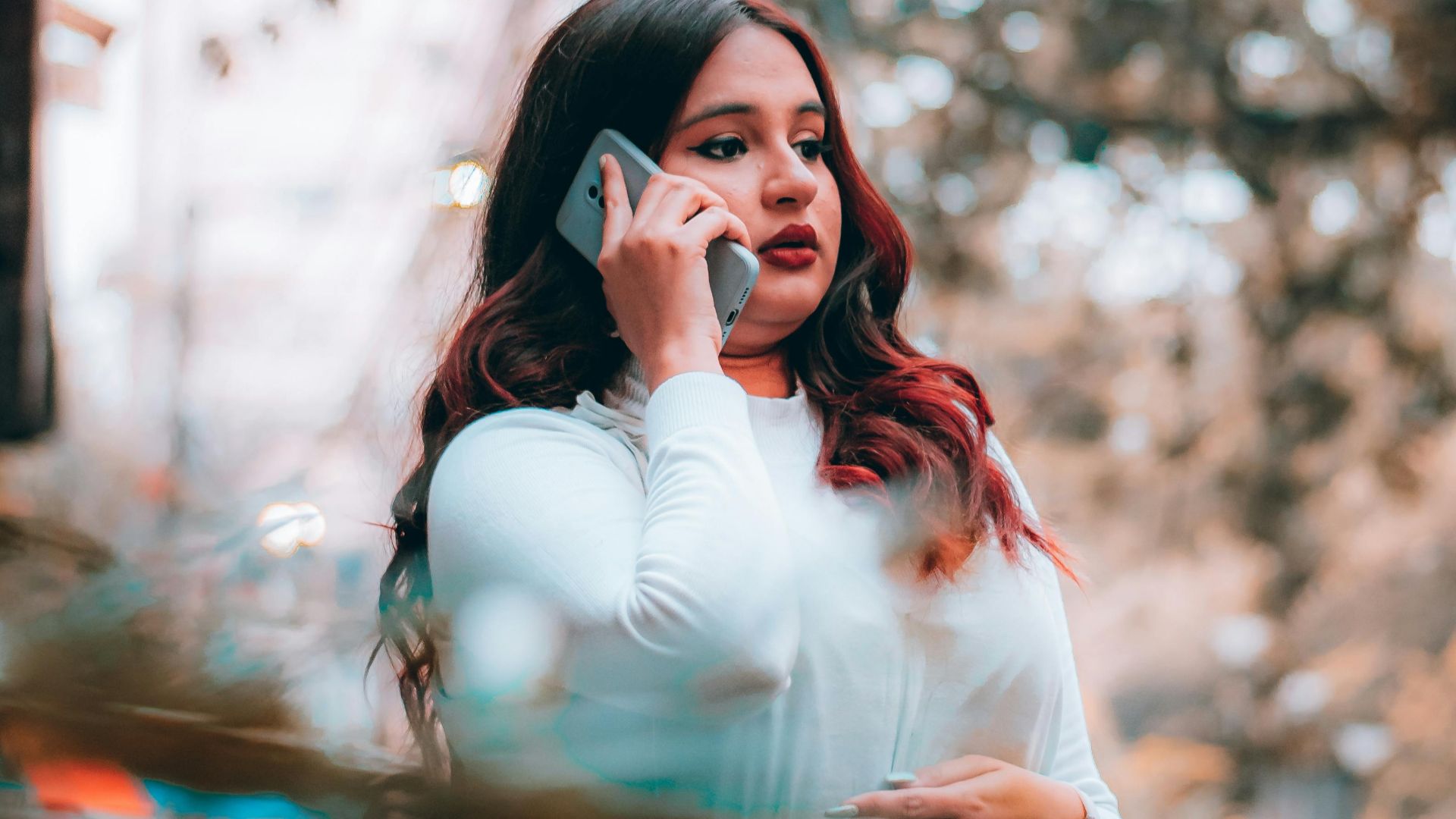 A young woman in a white dress using her smartphone outdoors on a sunny day.