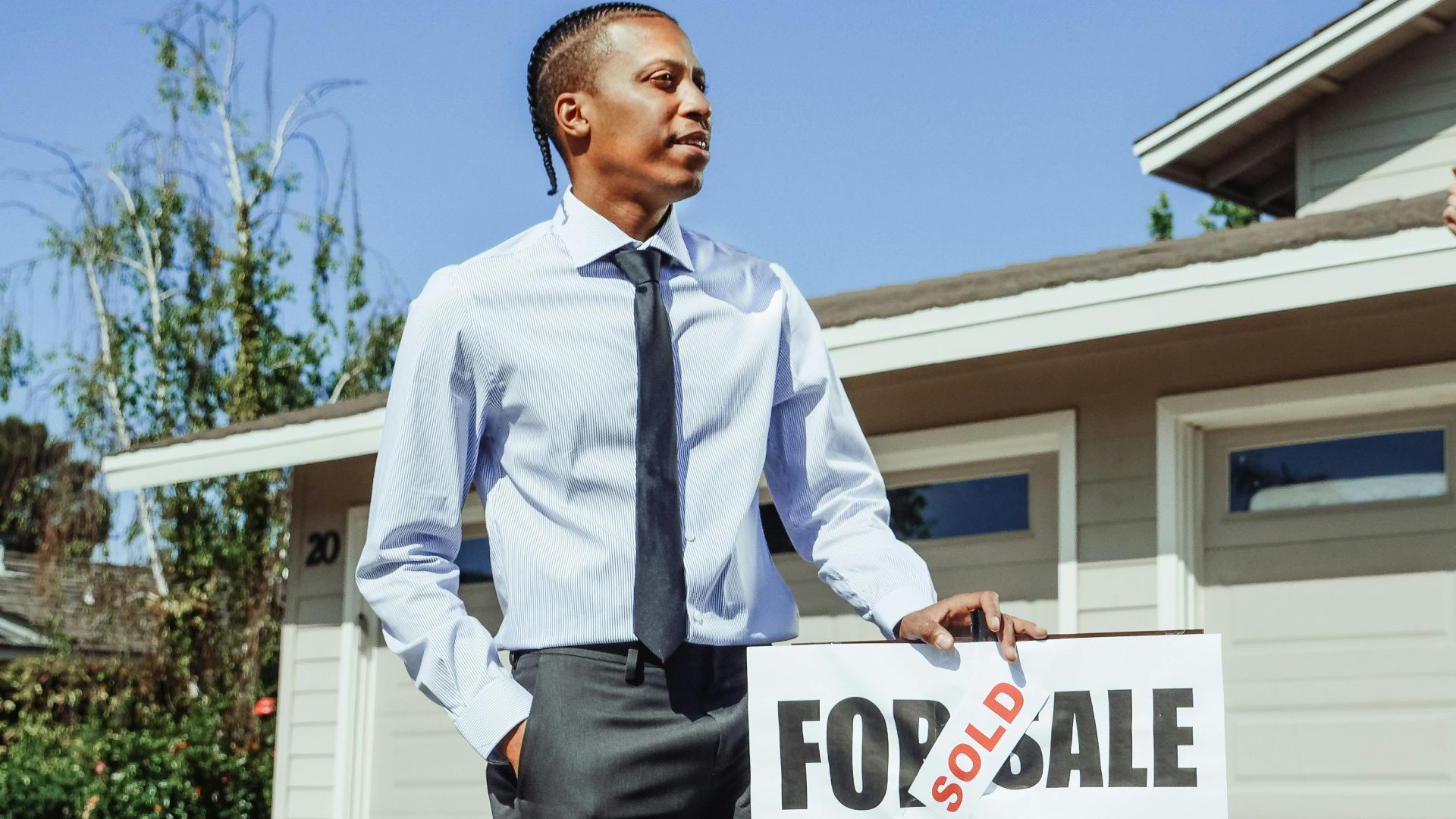 Real estate agent presenting a sold sign in front of a residential property.