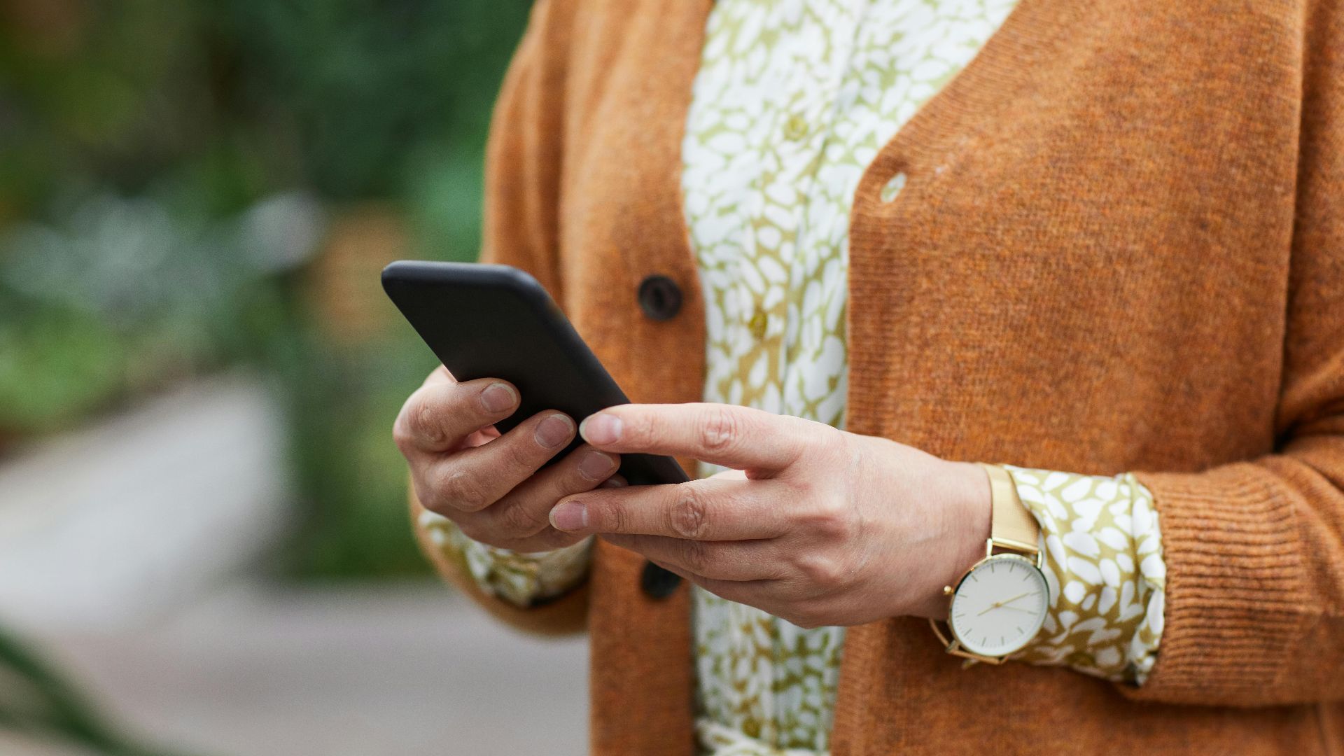 Elderly person's hands holding a smartphone in a casual setting, wearing a watch.