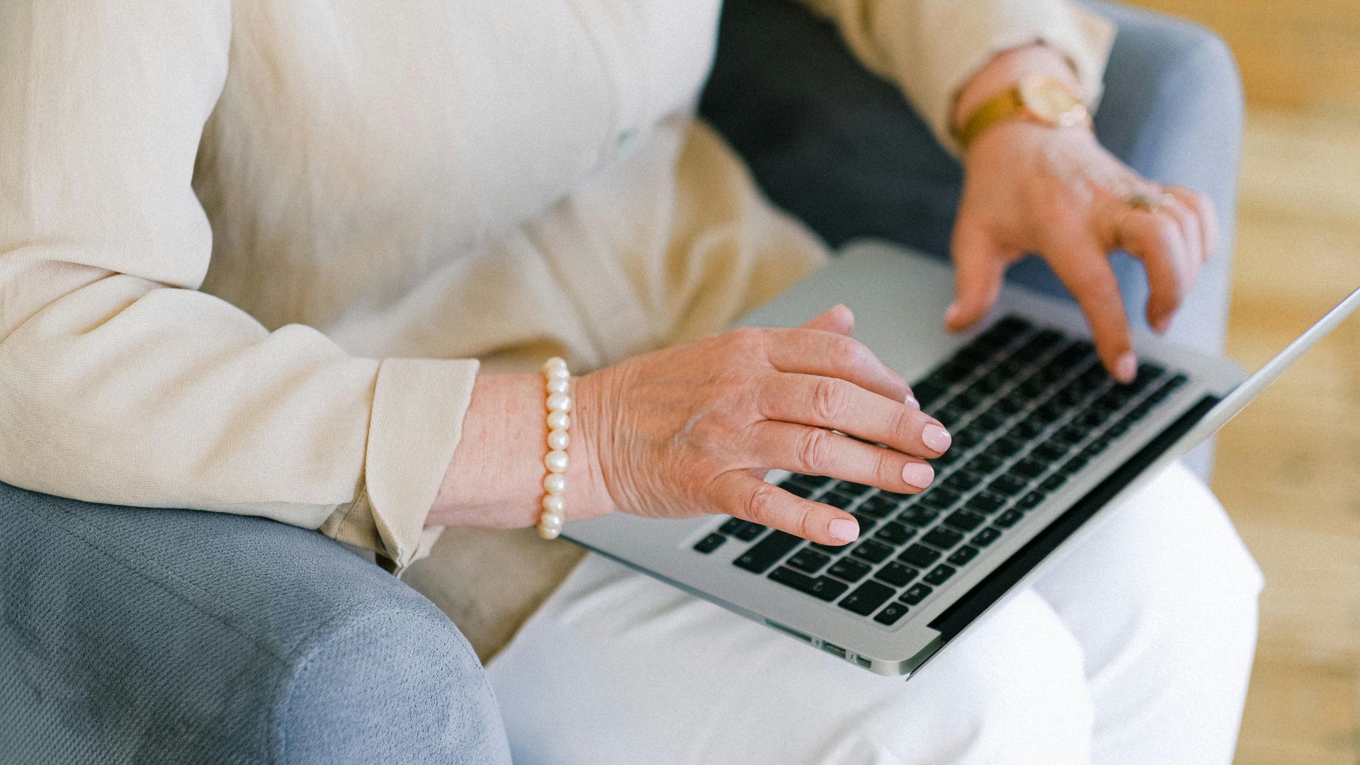 From above of crop anonymous elderly female typing information for report on netbook while resting in armchair in living room