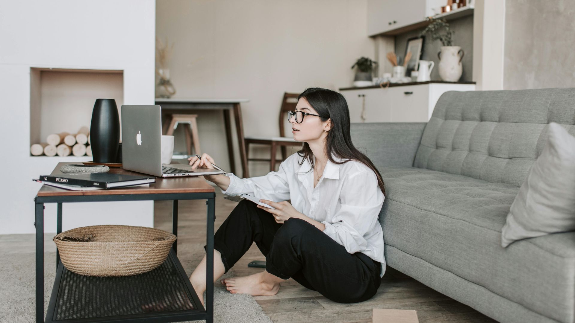 Asian woman working on laptop from cozy living room, showcasing modern home office setup.