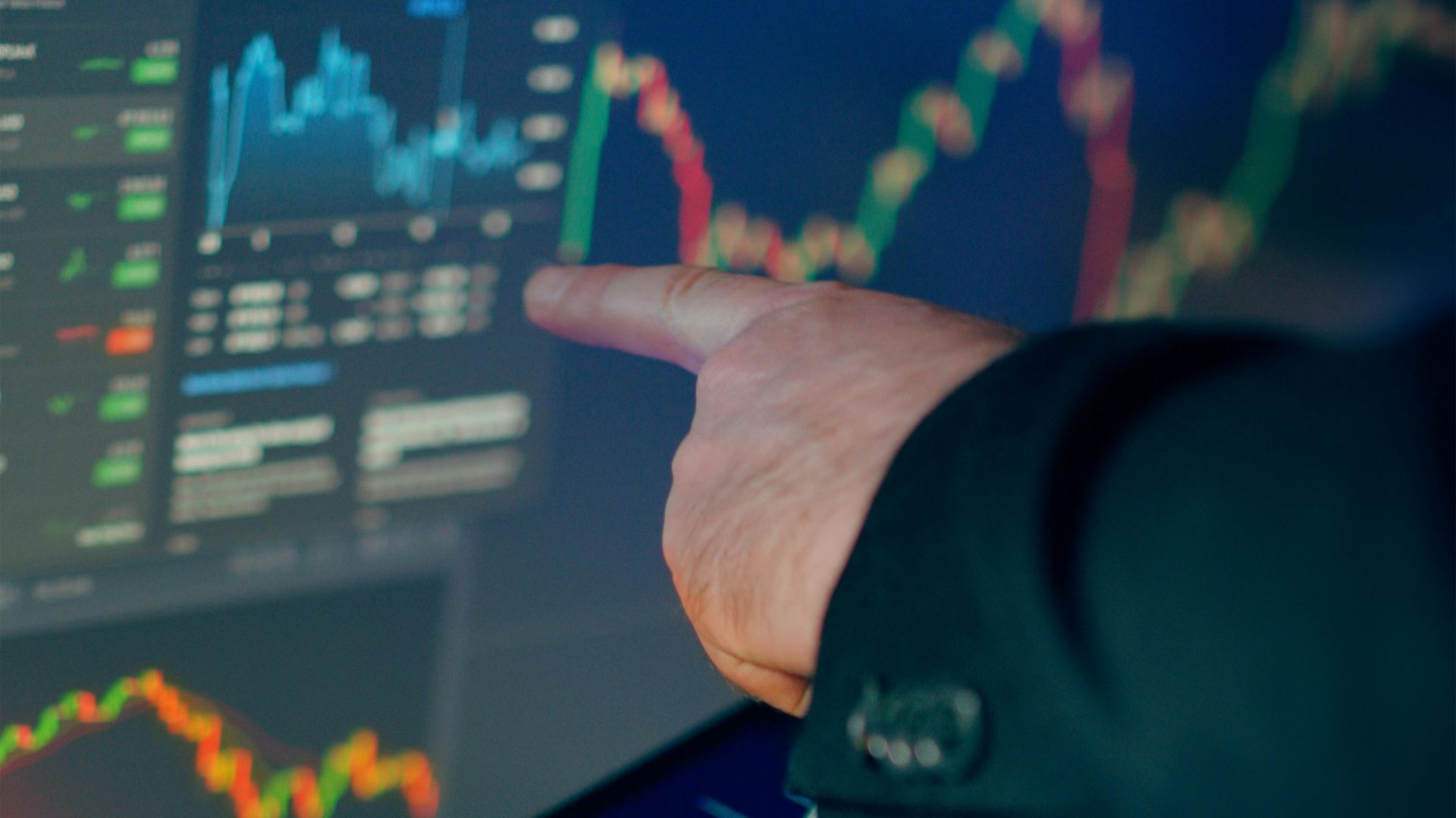 A business professional examines financial charts on a tablet and monitor for investment strategy.