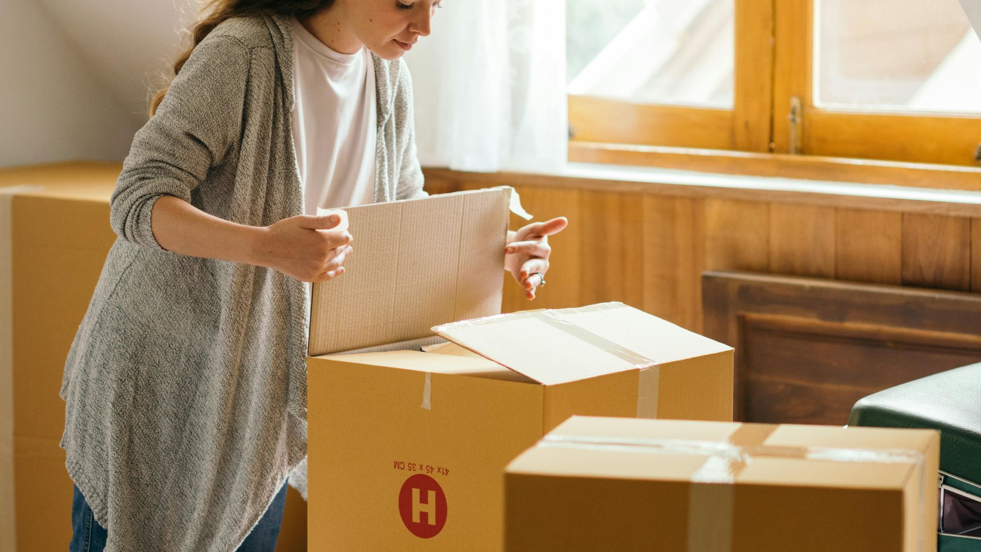 Serious female with curly hair carefully packing stuff in boxes preparing for moving out light apartment