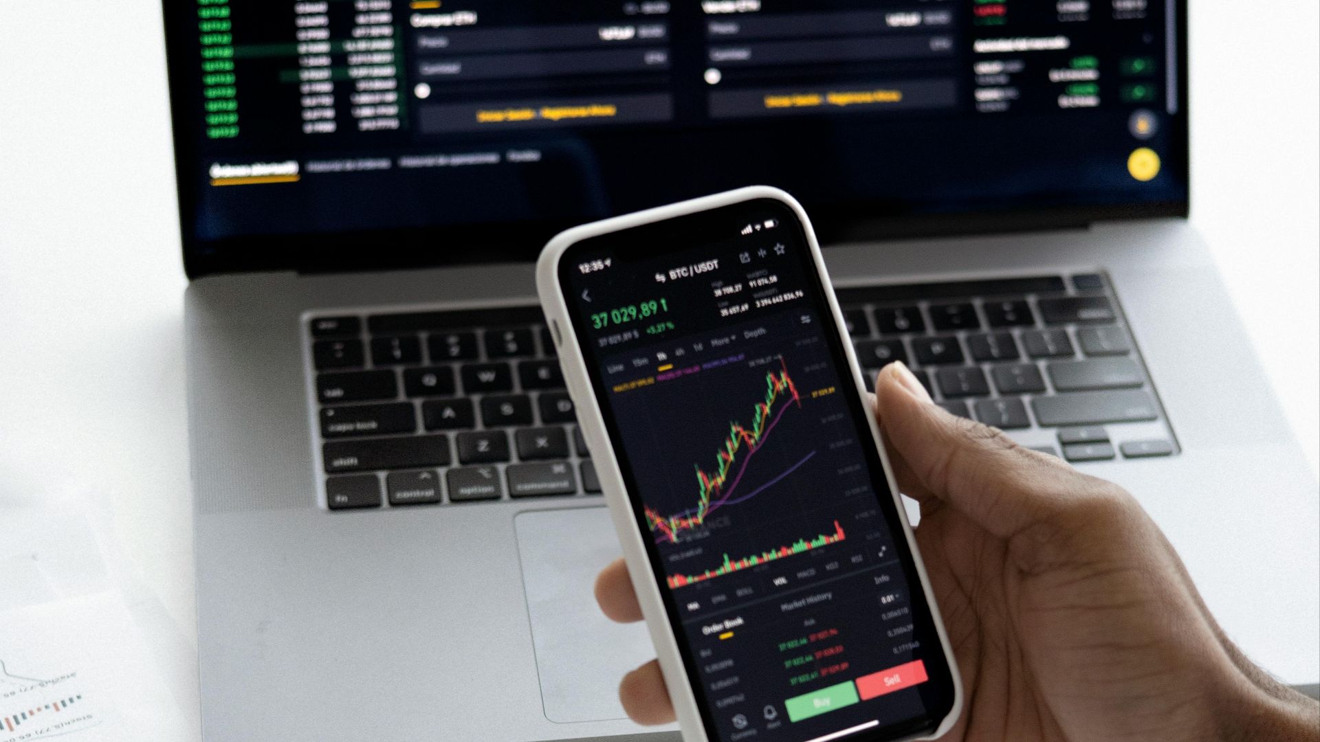 Person analyzing stock market trends on smartphone with laptop background