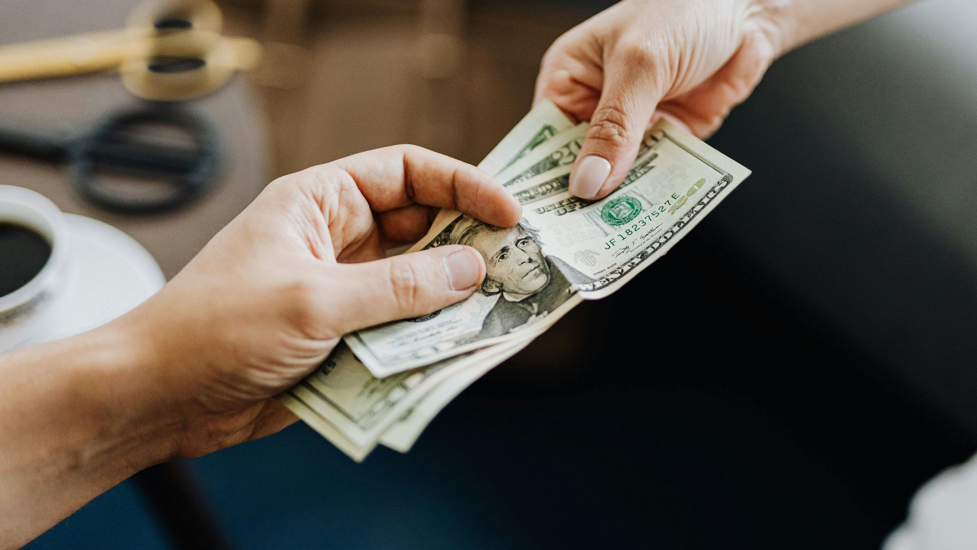 A close-up image of hands exchanging US dollar bills, symbolizing financial transaction or payment.