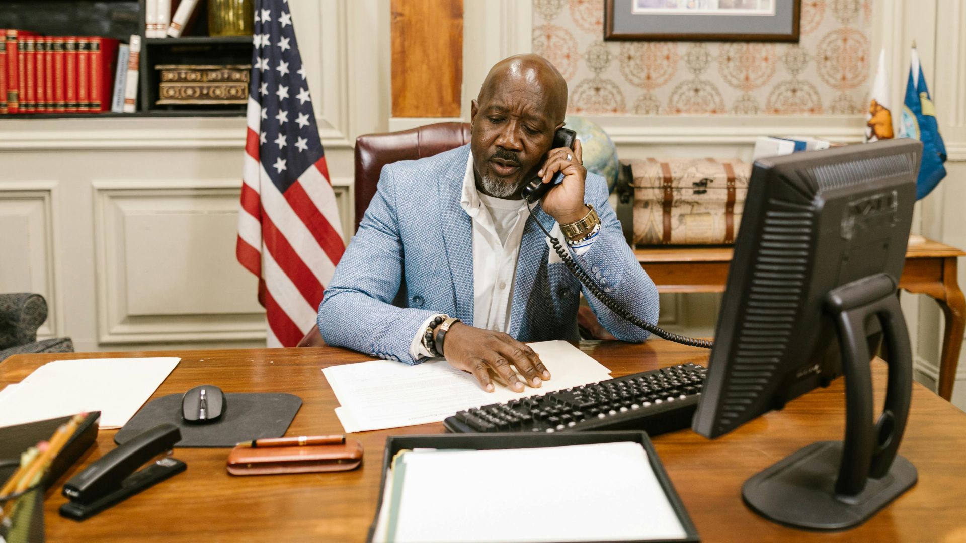Businessman using phone in a classic office setting with an American flag and computer.