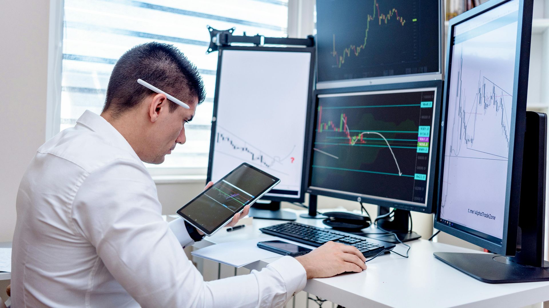 Professional analyzing stock market graphs on multiple monitors at work desk.