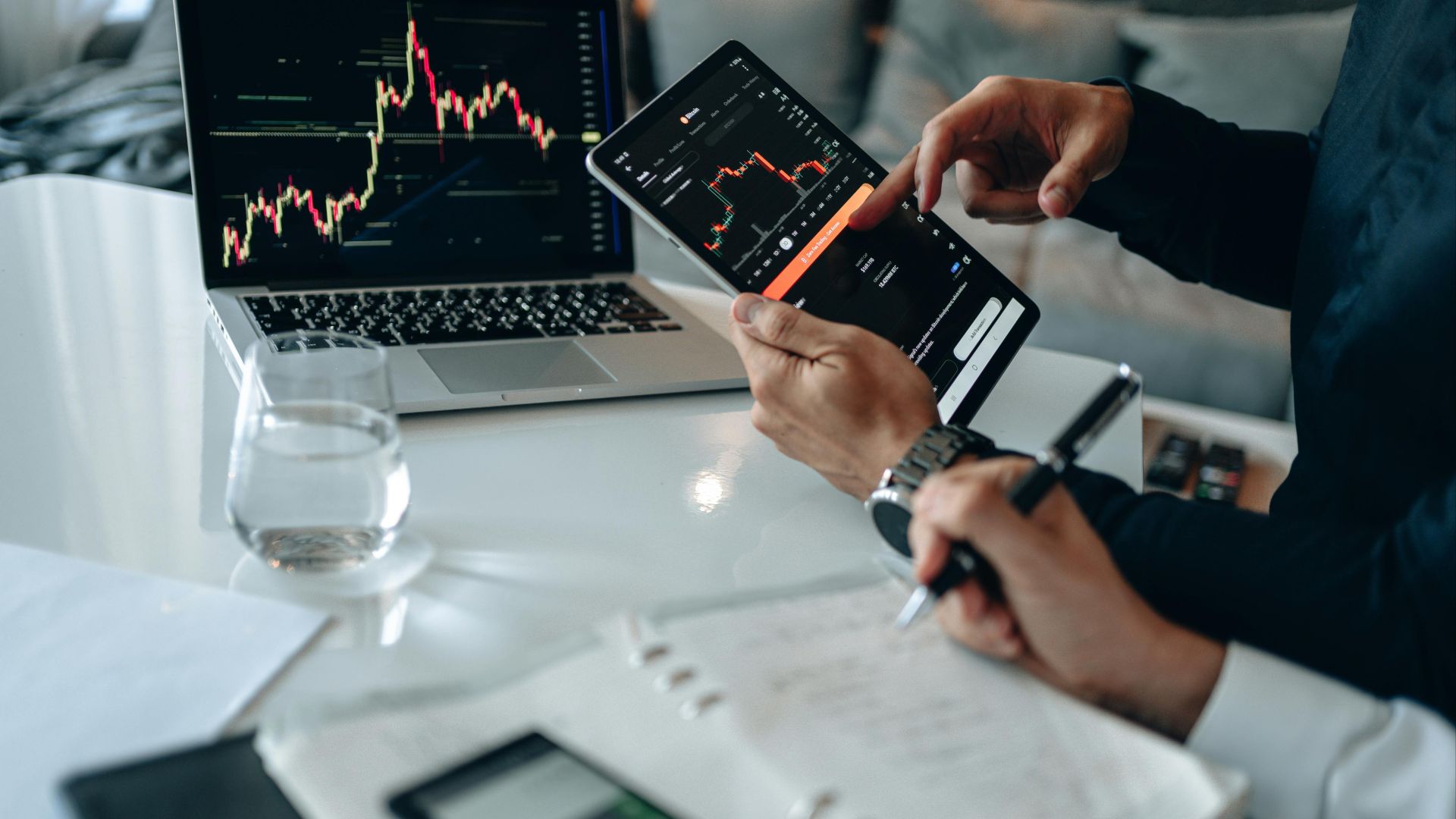 Business professionals reviewing financial charts on digital devices in a modern office setting.