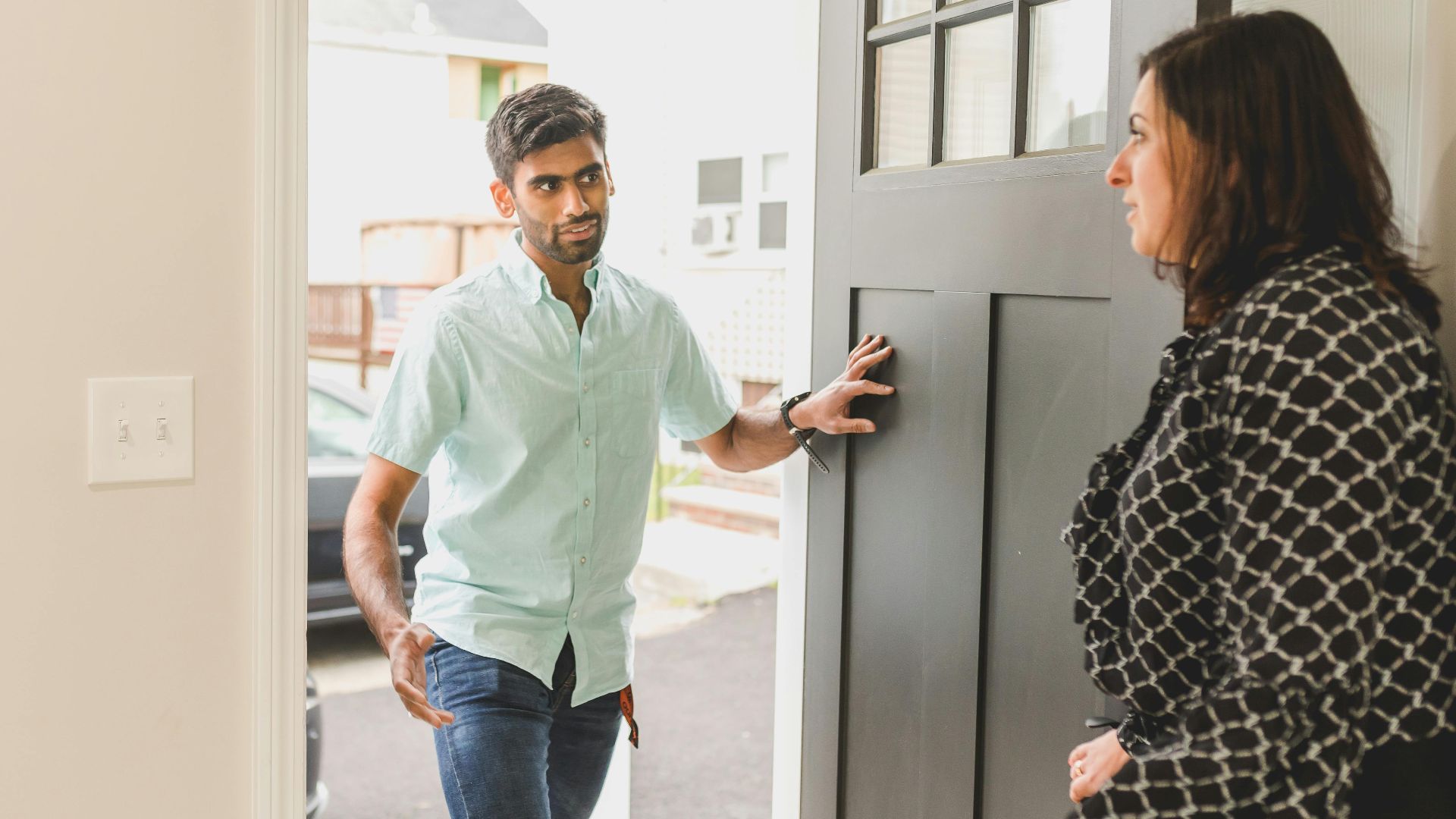 A man enters a home, conversing with a woman standing nearby in a casual setting.