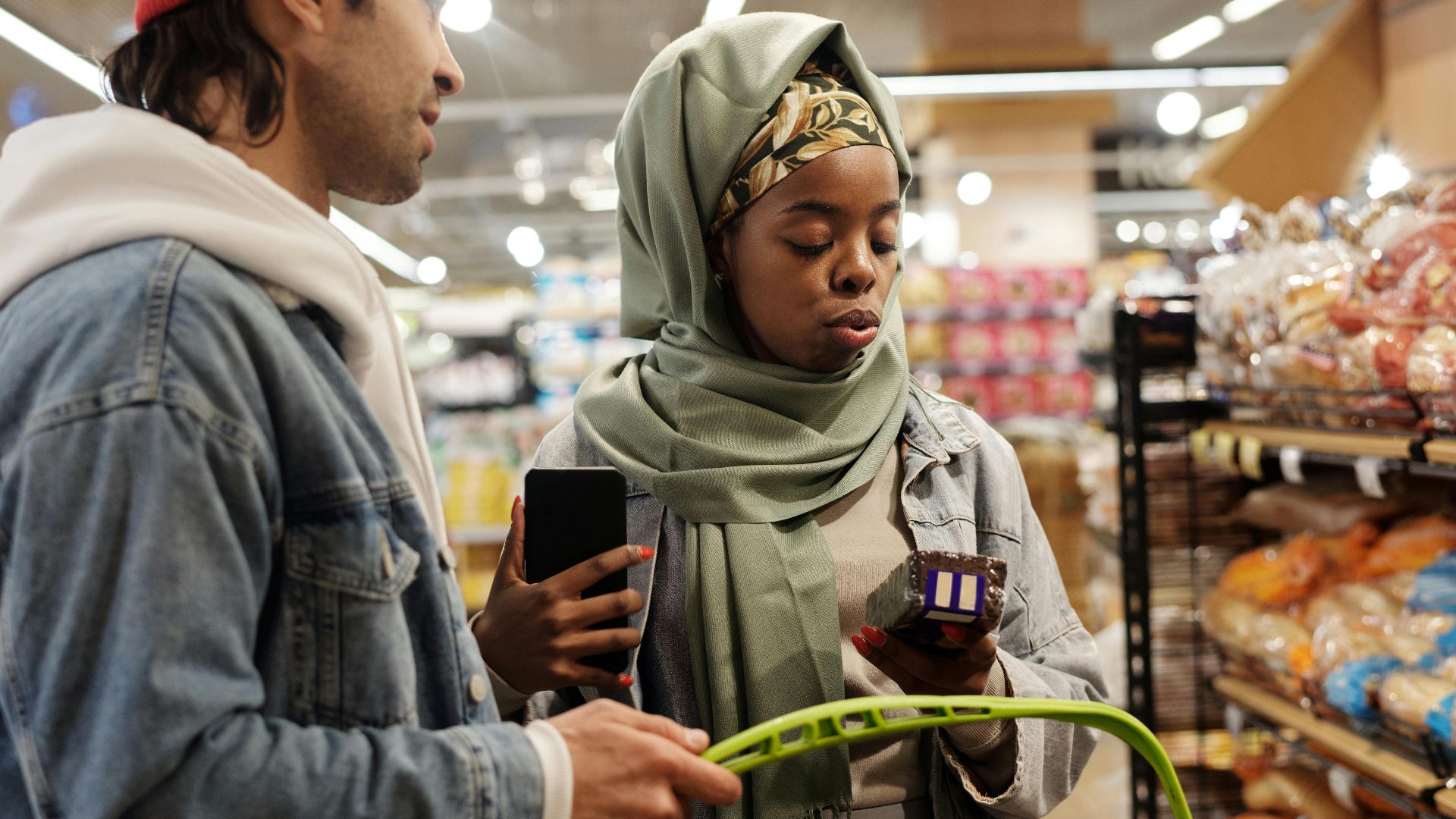 A young couple shops for groceries in a supermarket, checking items with a smartphone.