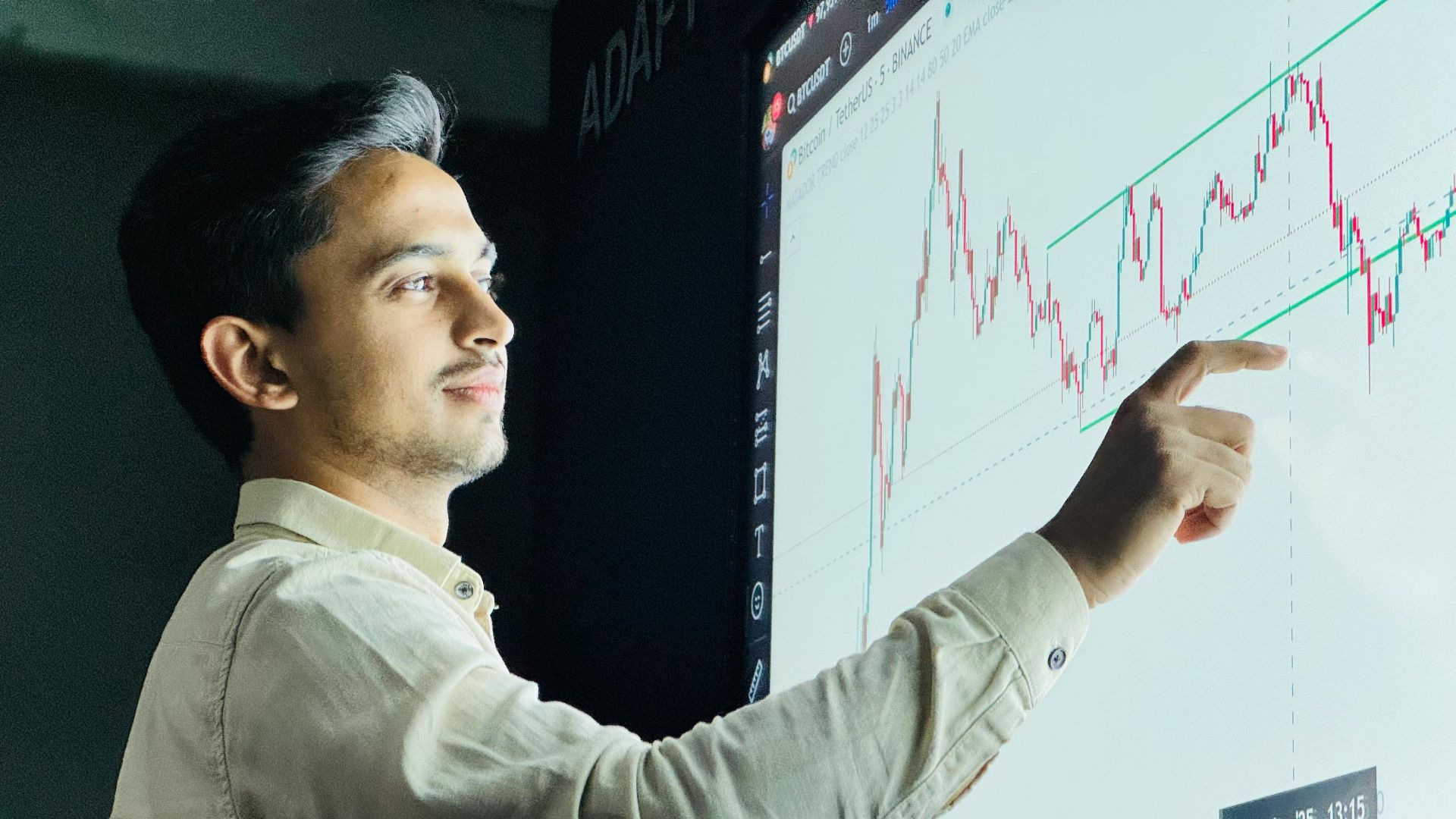 Man analyzing stock market graph on a digital board with a focused expression.
