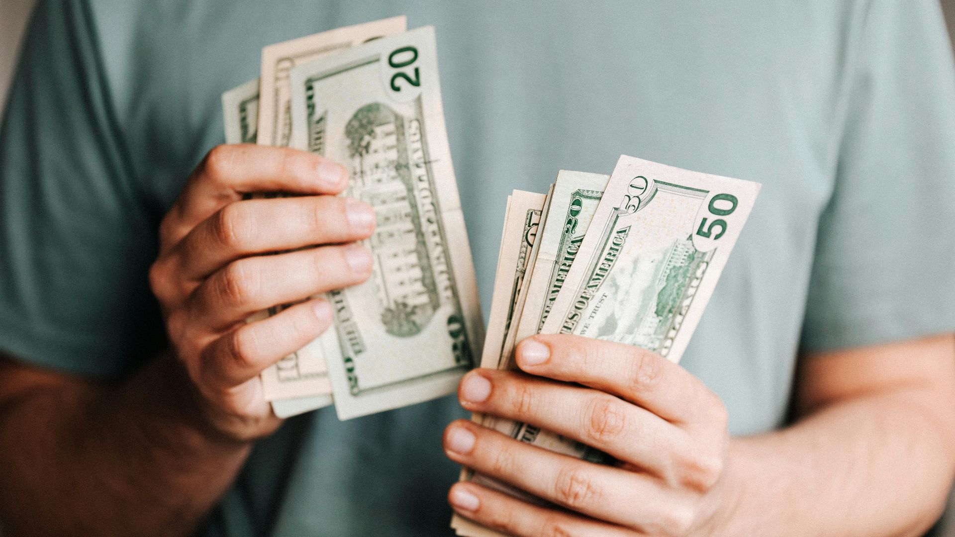 Crop anonymous male in casual tshirt holding dollar banknotes counting money with hands