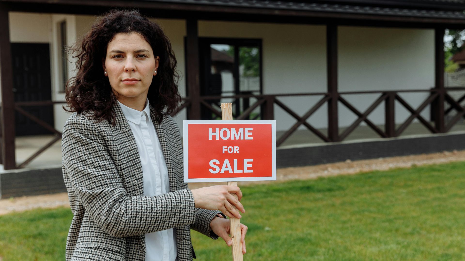 Confident real estate agent with sale sign in front of a house.