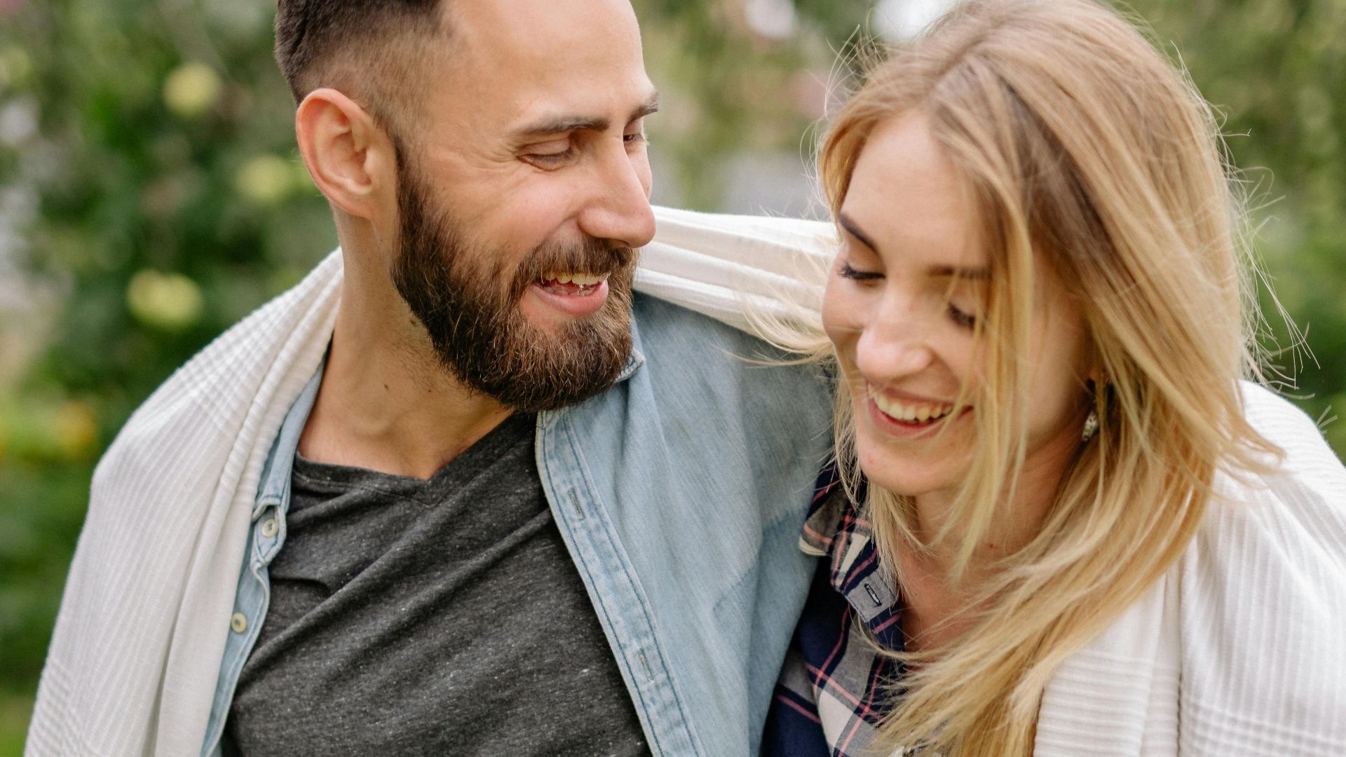 Smiling couple enjoying leisure time wrapped in blanket outdoors during daytime.