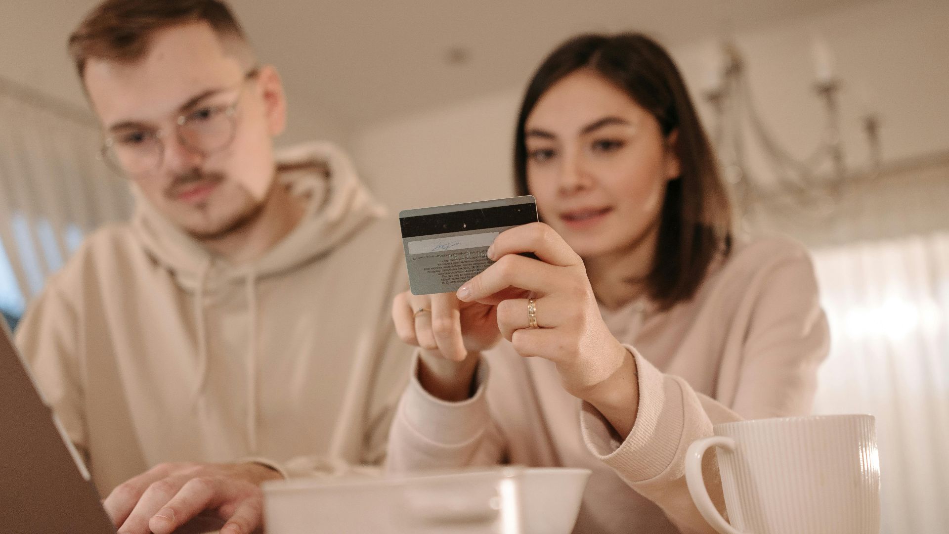 Young couple shopping online using a laptop and credit card at home, enjoying a cozy indoor setting.