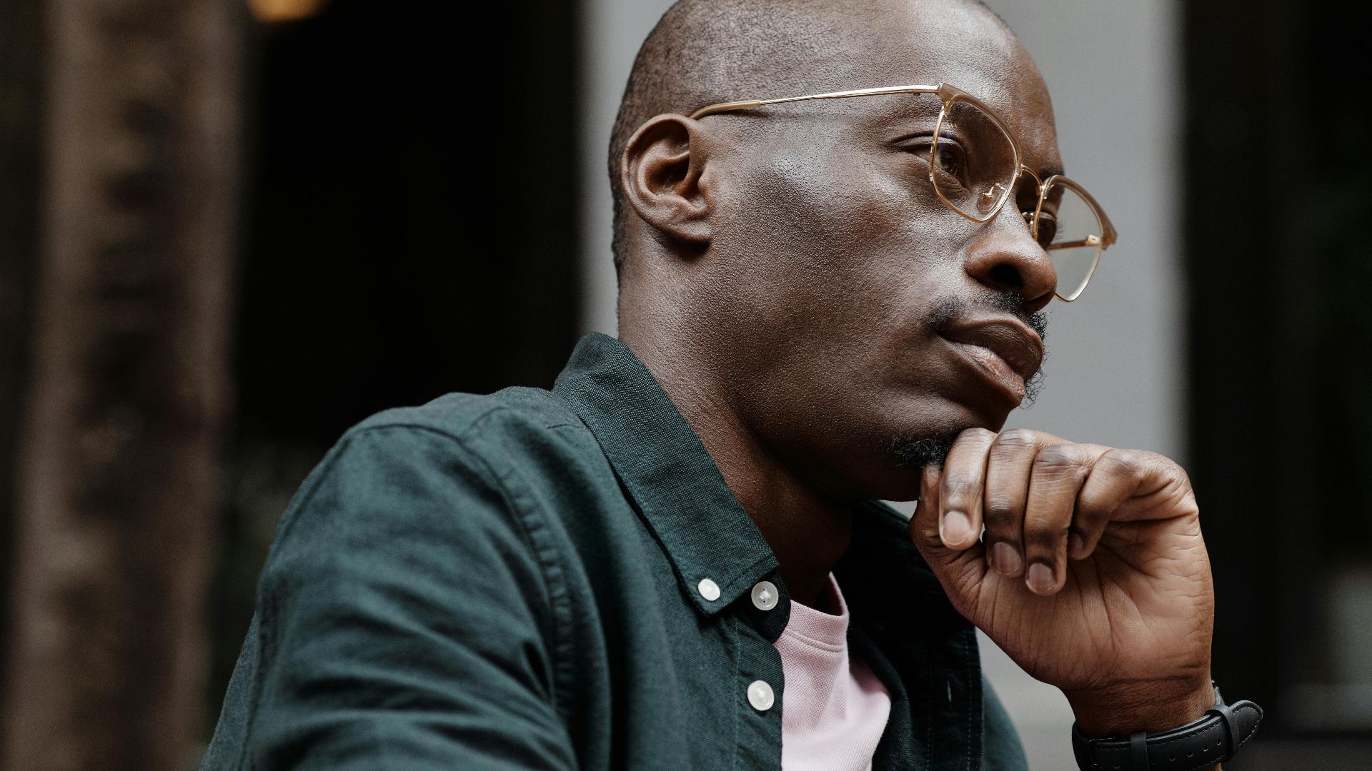 Thoughtful man with glasses sitting outdoors in contemplation.