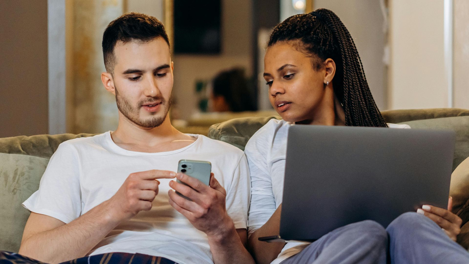 A couple sitting together on a couch, using a laptop and smartphone, enjoying a cozy moment.