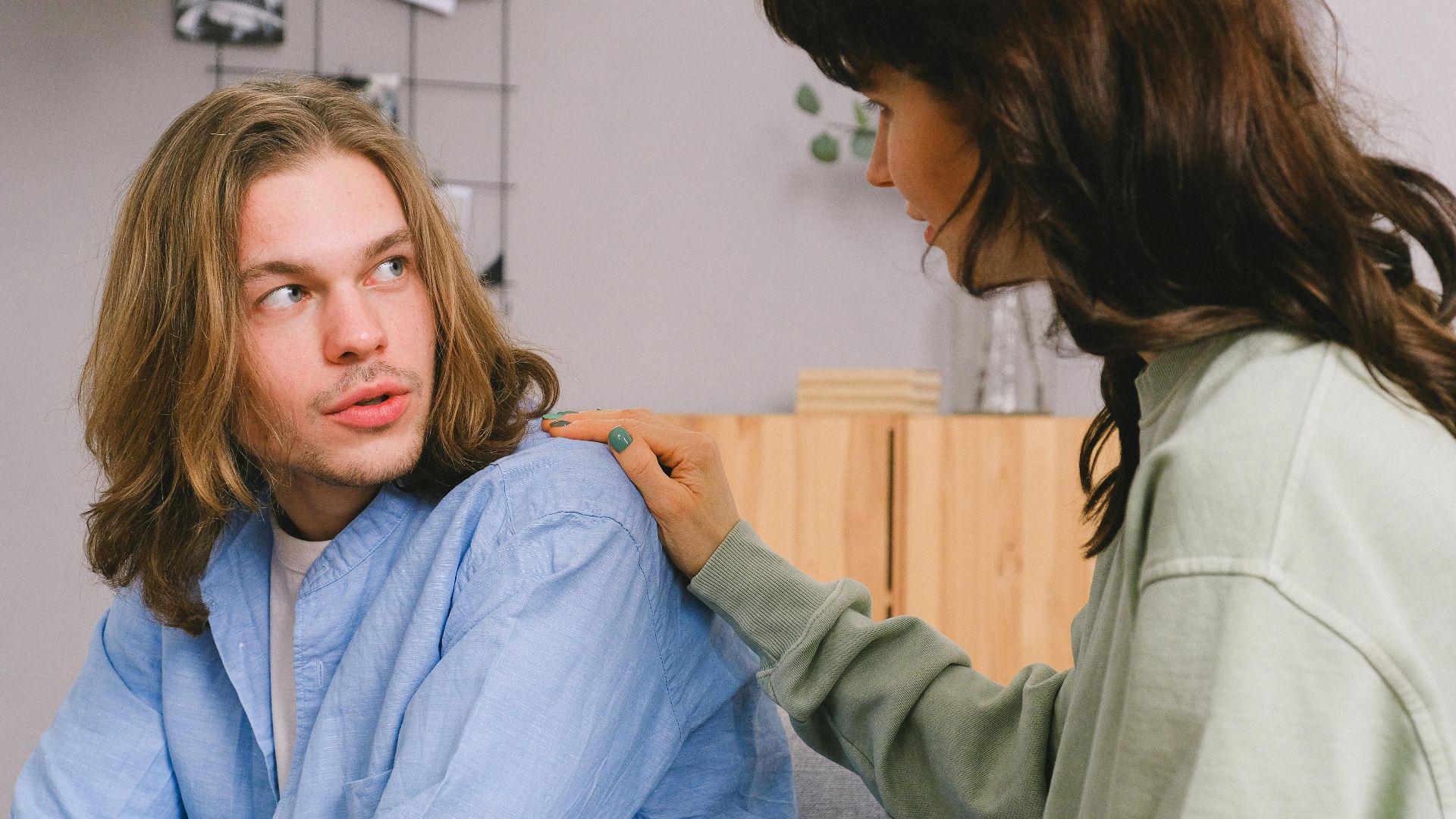 Concentrated woman talking and touching shoulder of pensive male in light room in daytime