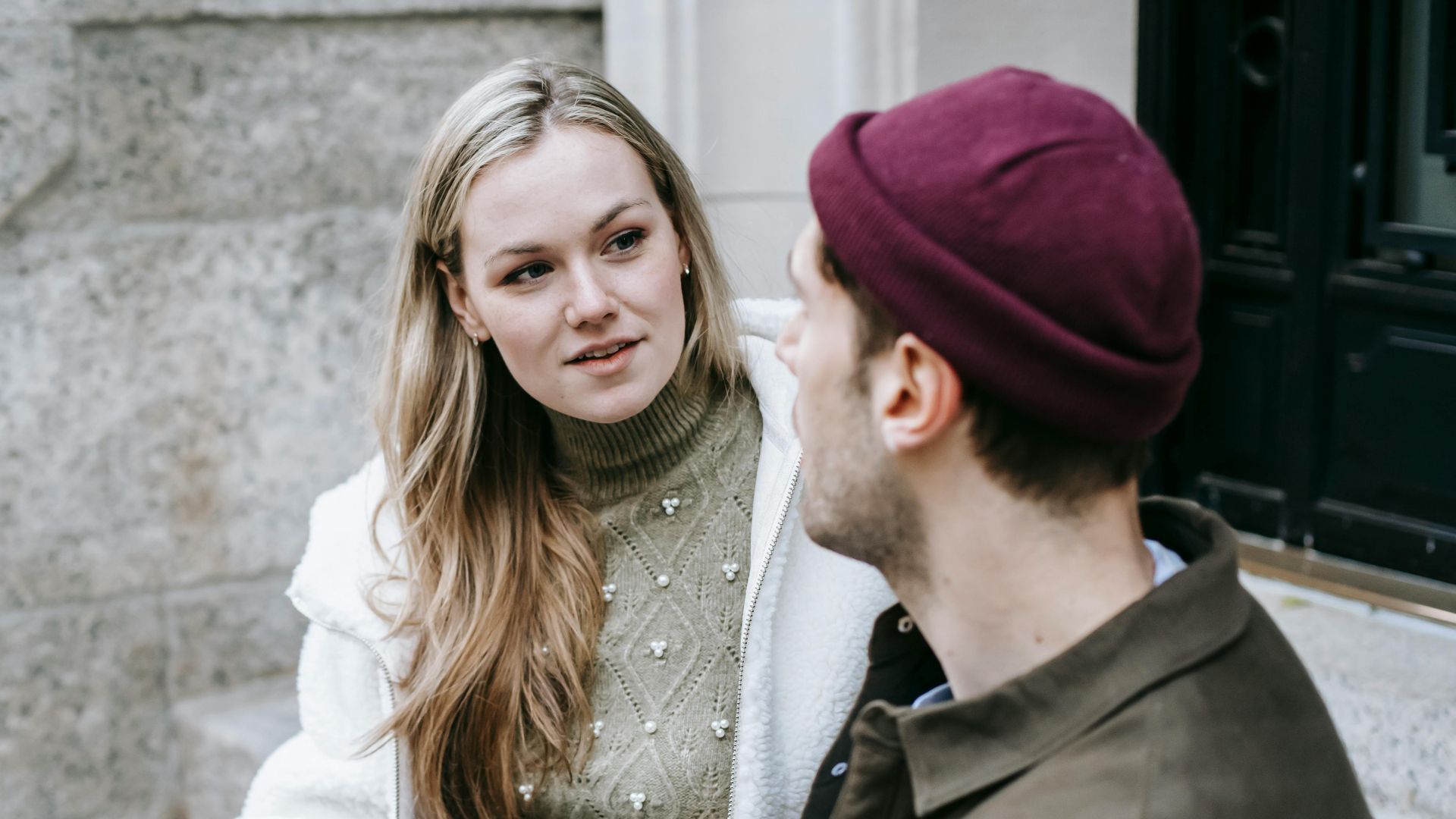 Man and woman talking sitting on steps outside house and having hot beverage in paper cups