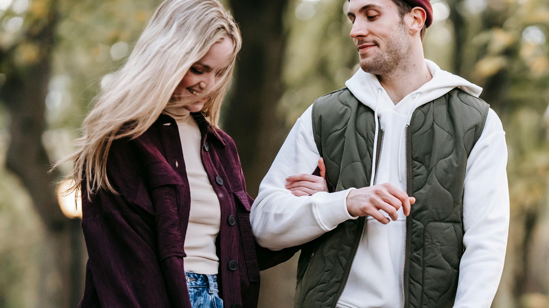 Crop couple in casual outfit with fresh white roses promenading on blurred background of park with green trees