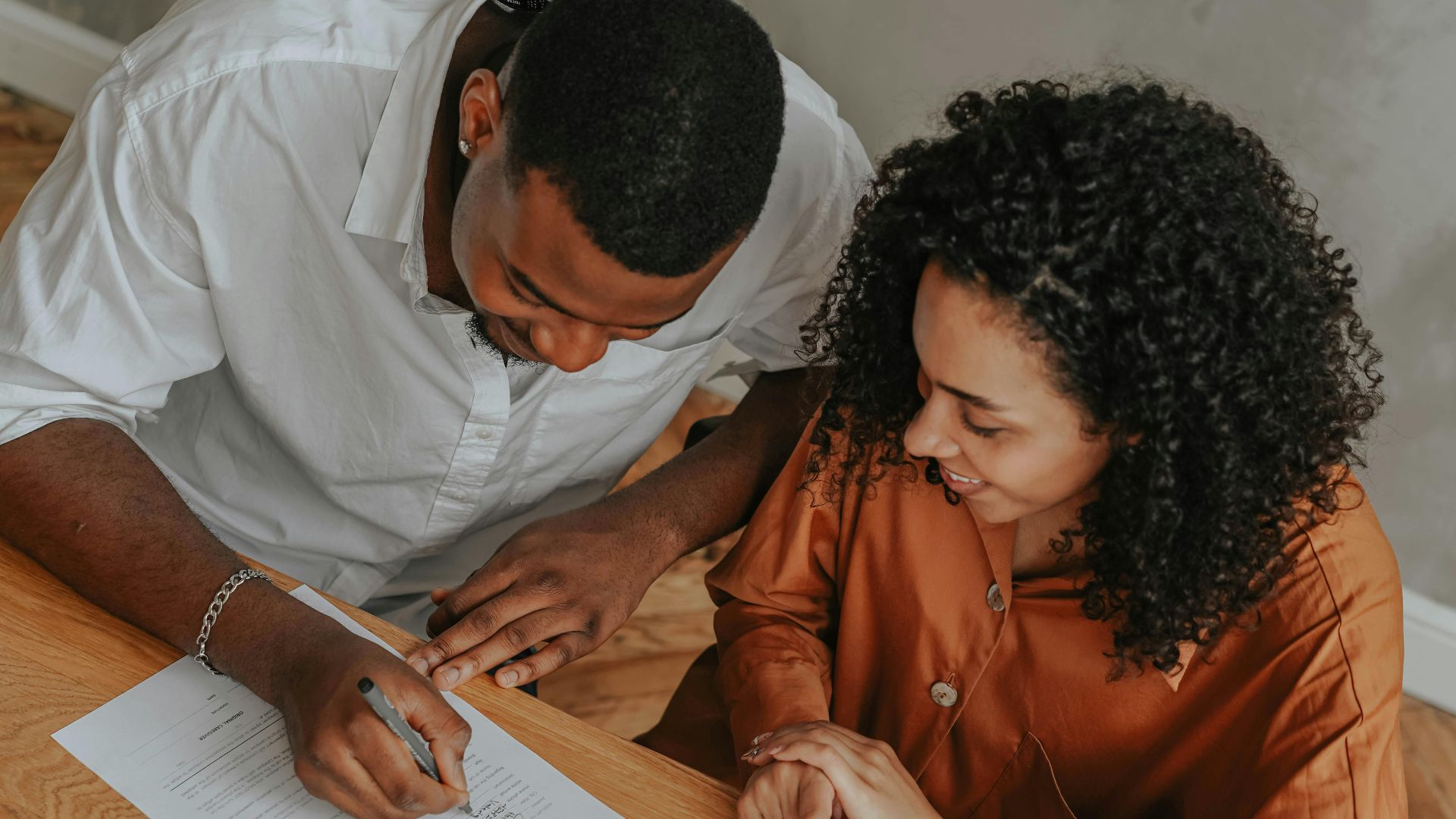 A couple signing an adoption certificate at a table, viewed from above.