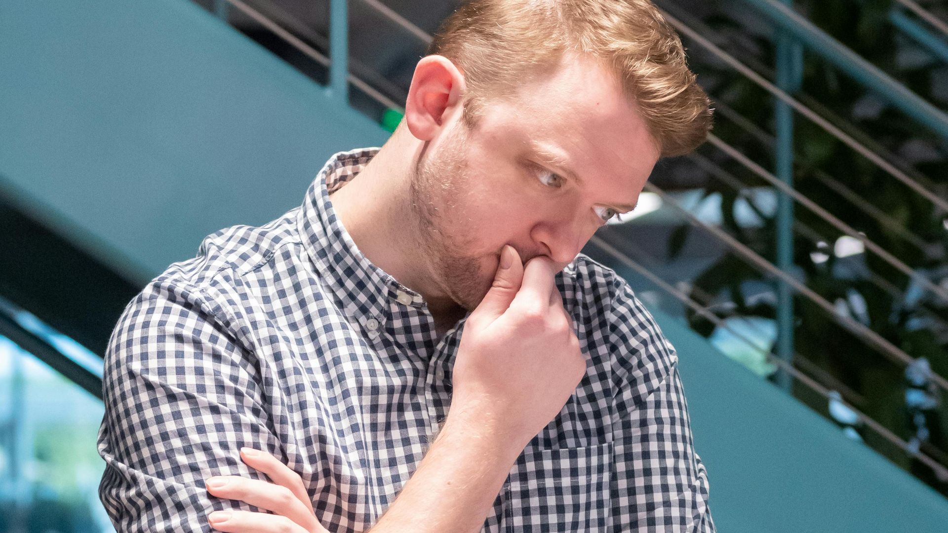 Man in a plaid shirt deep in thought while working in a modern office.
