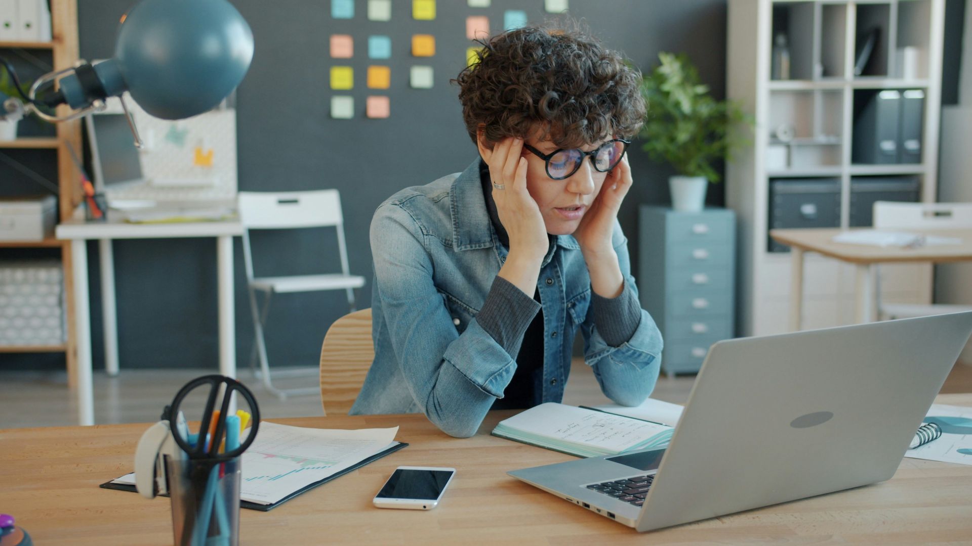 A person looking stressed at a laptop in an office.