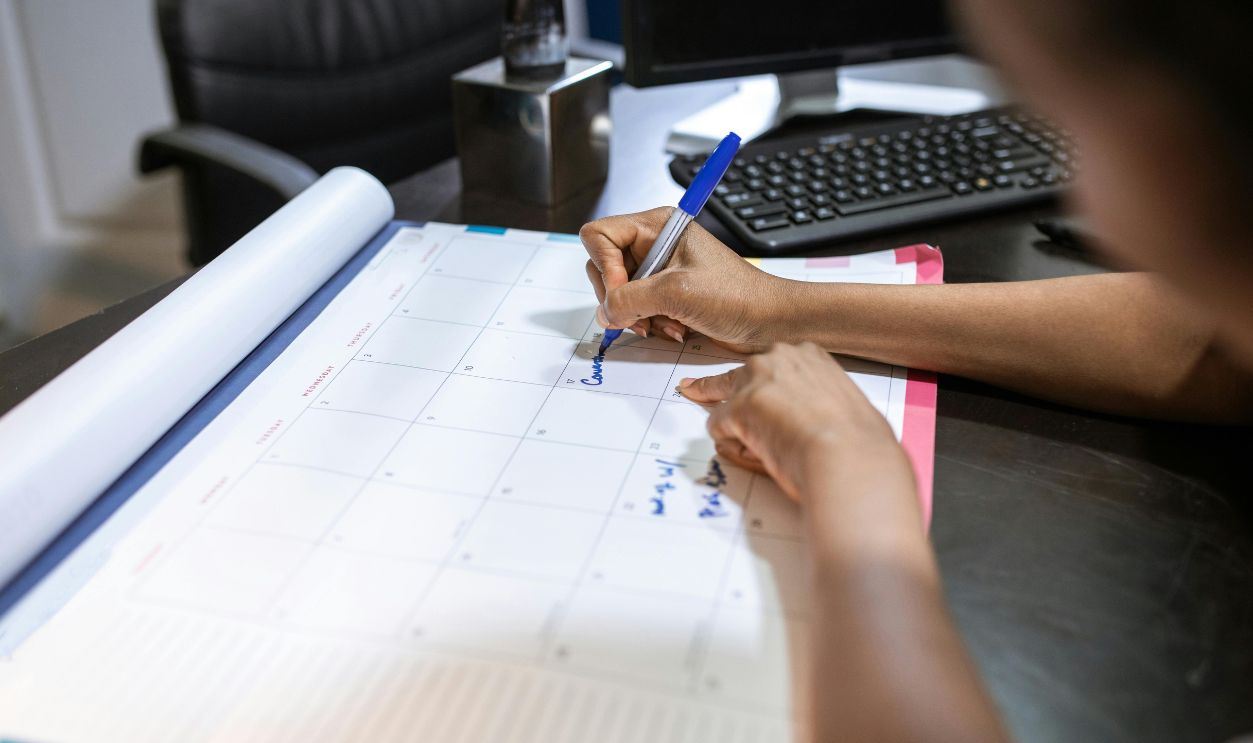 Close-up of a woman planning her schedule on a desk calendar in an office setting.