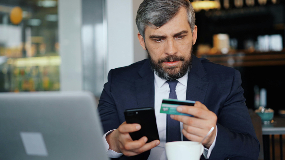 A businessman at a cafe, frowning at his credit card.