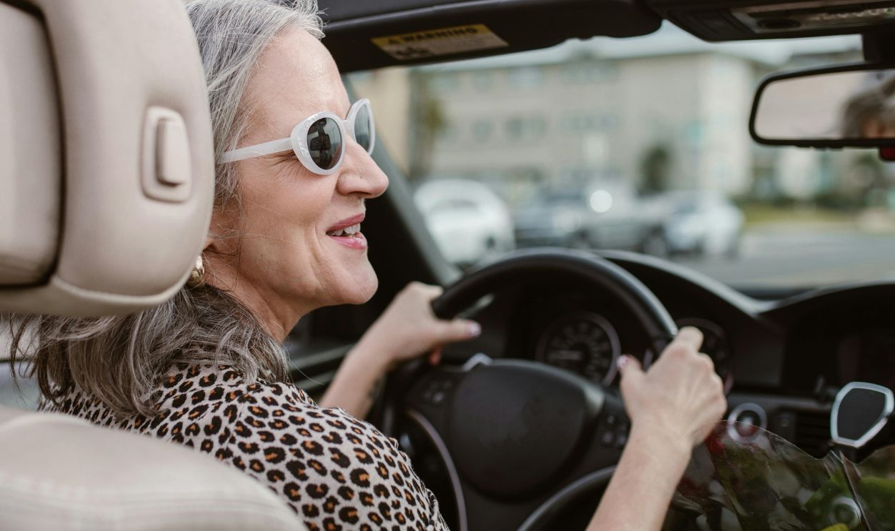 Senior woman driving a convertible, smiling and wearing sunglasses