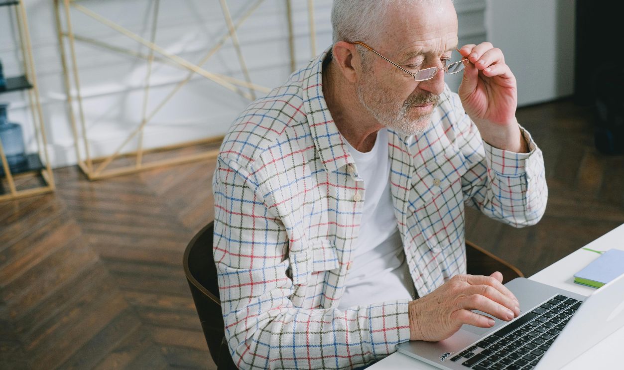 Elderly man wearing glasses focused on working at a laptop