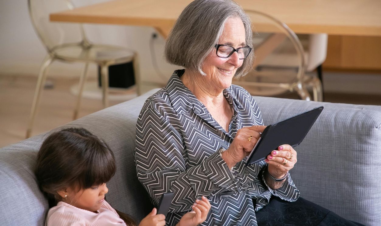 A senior woman and a young girl on a sofa interacting with a tablet