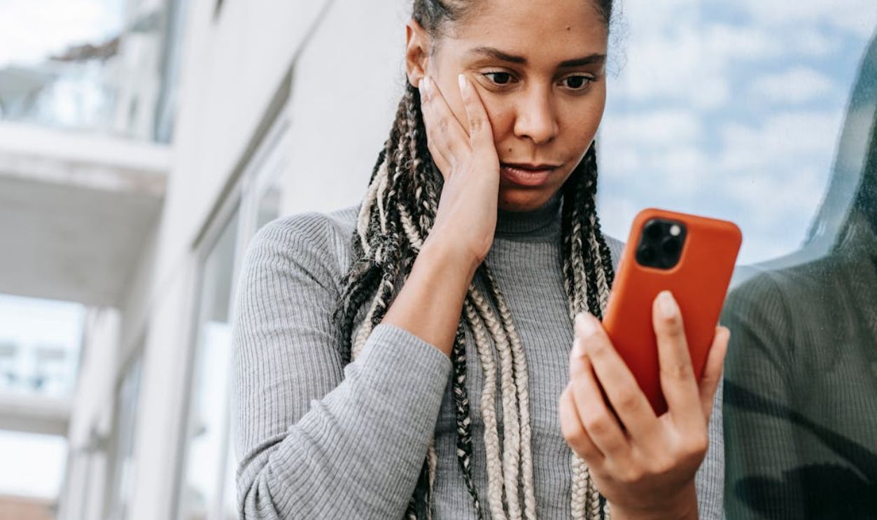 A woman looks concerned while browsing her smartphone outside on a street