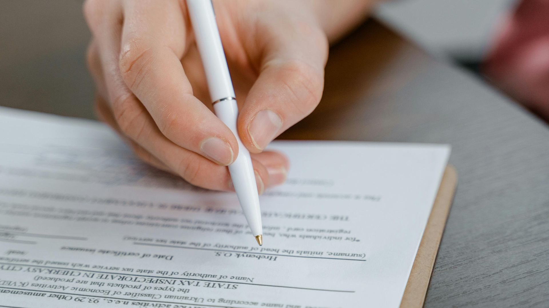 A hand holding a pen signing a document, close-up shot with focus on the paper.